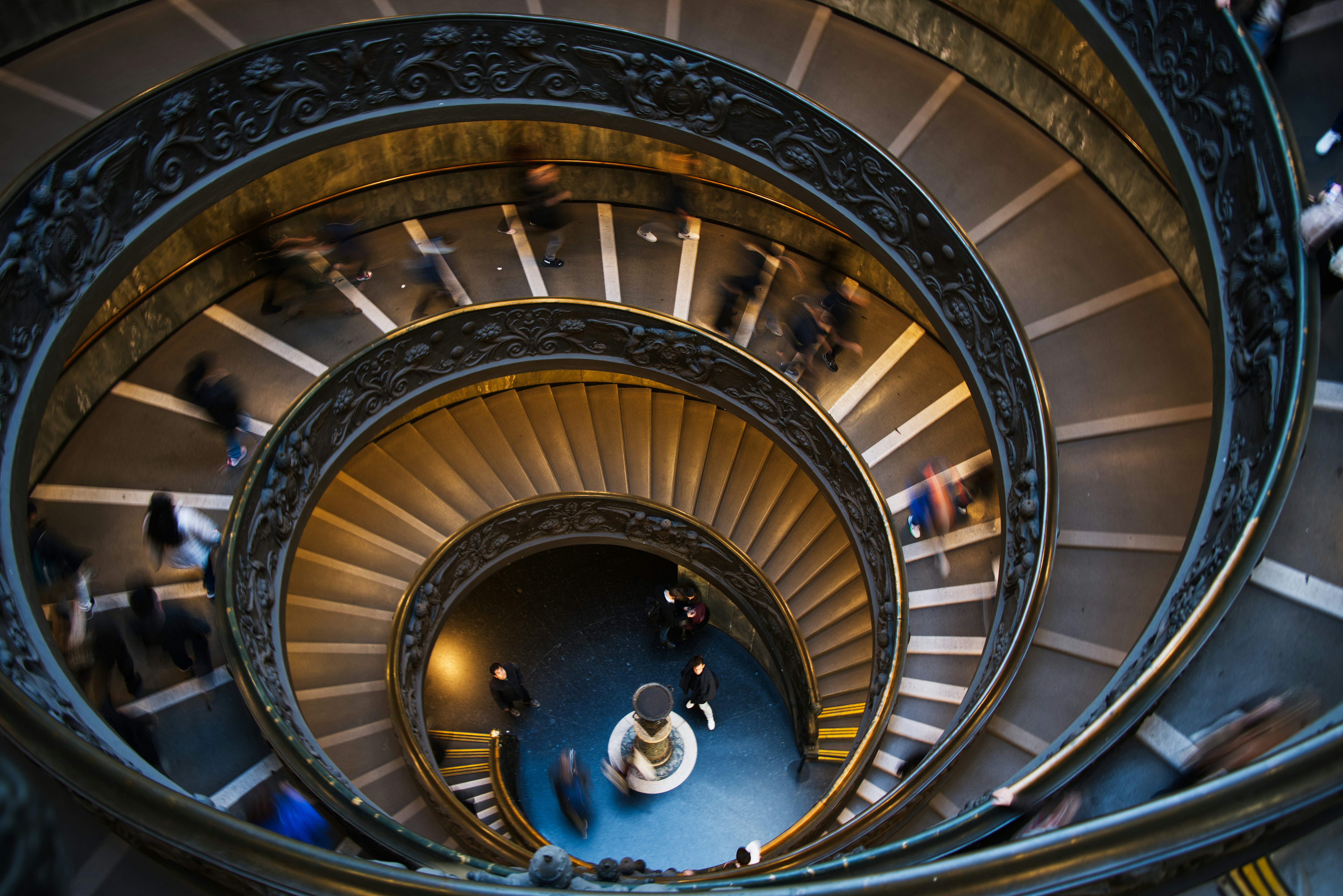 People ascend a spiral staircase in a museum.