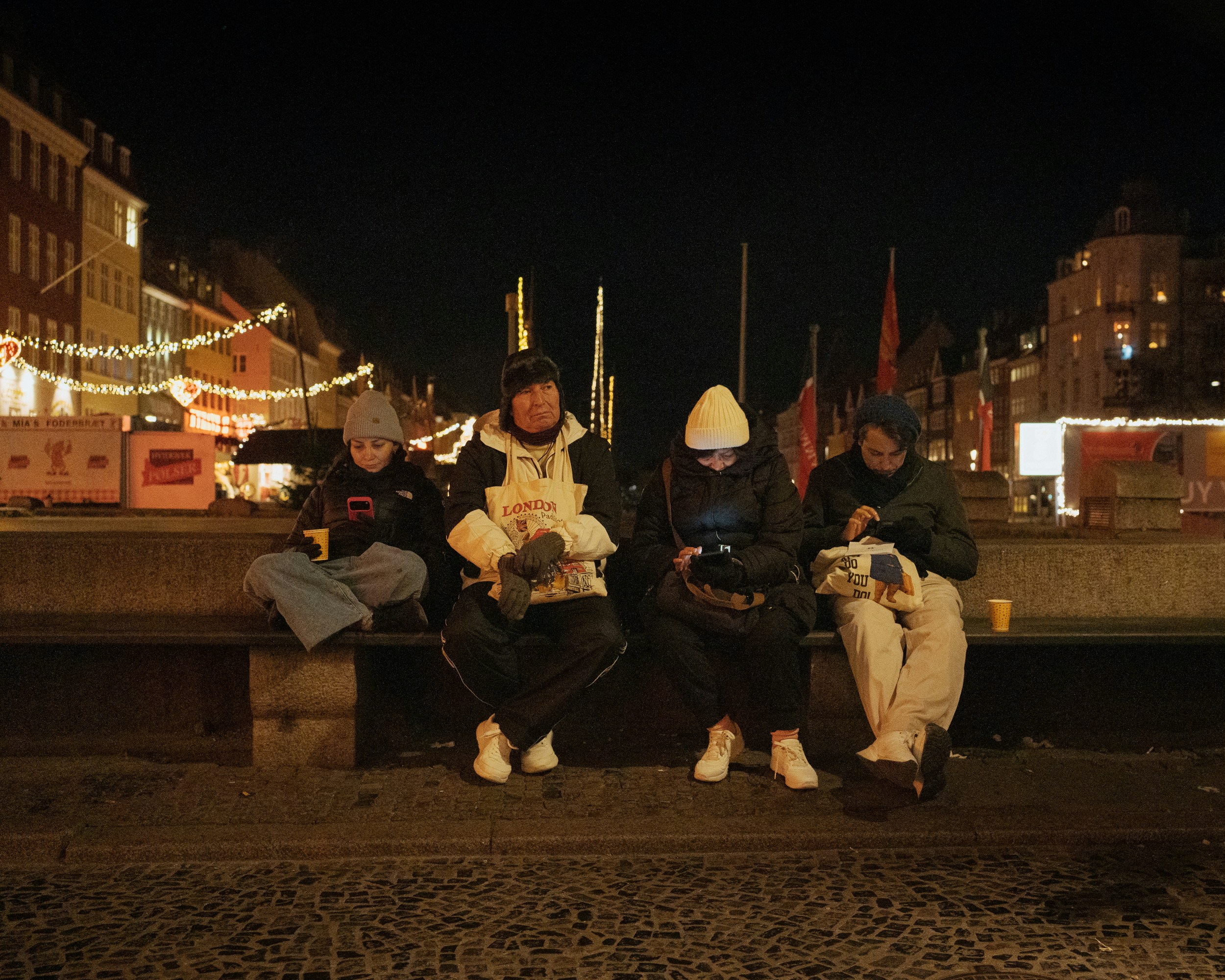 Four people sit on a bench at night.