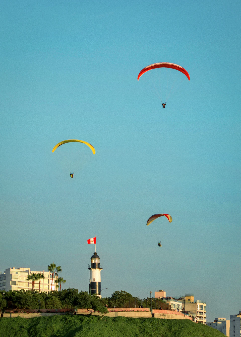 Three colorful paragliders soar through clear blue sky over cityscape in synchronized flight formations