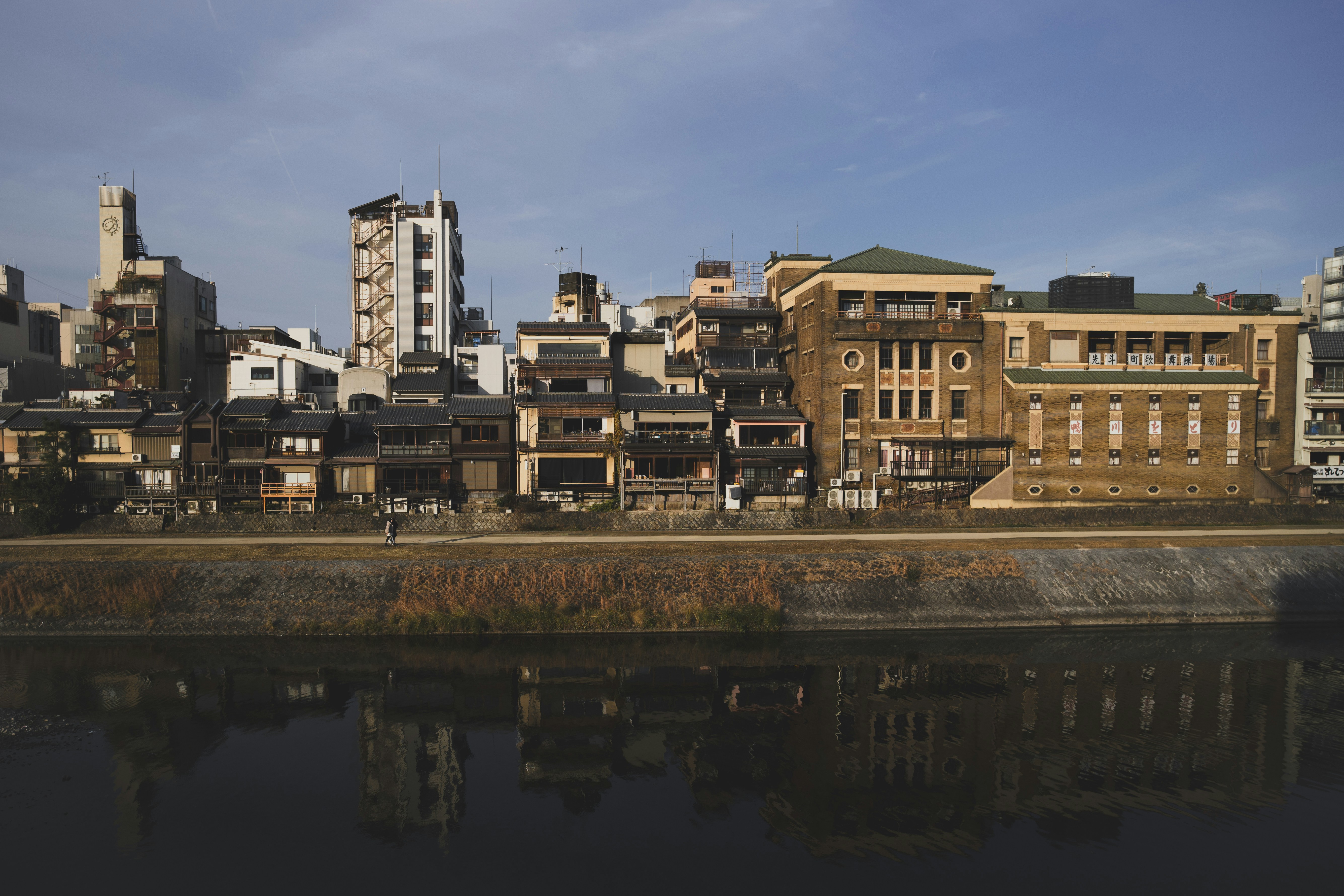 Edifícios margeiam uma margem de rio com reflexos na água.