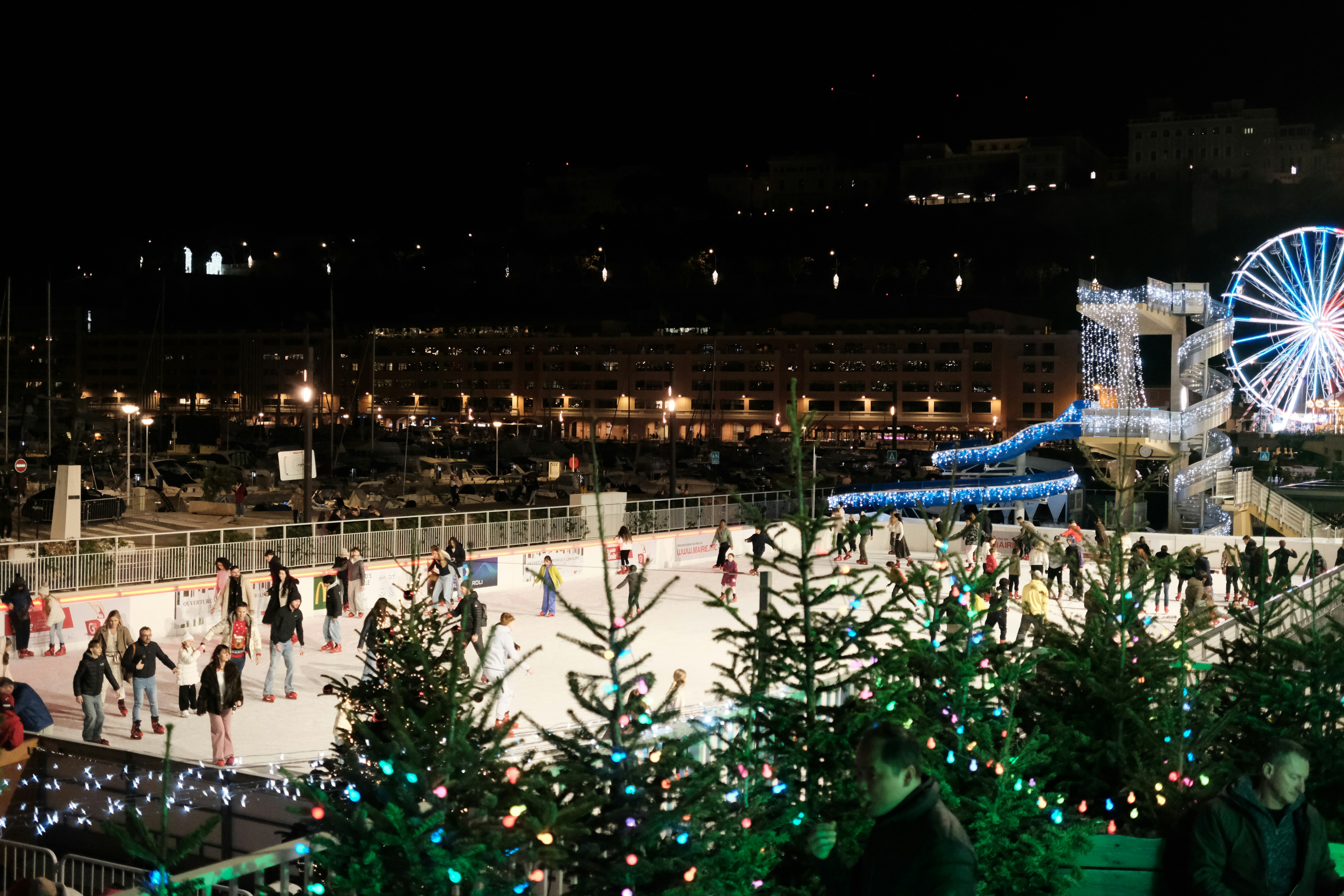 People ice skating at night with ferris wheel.