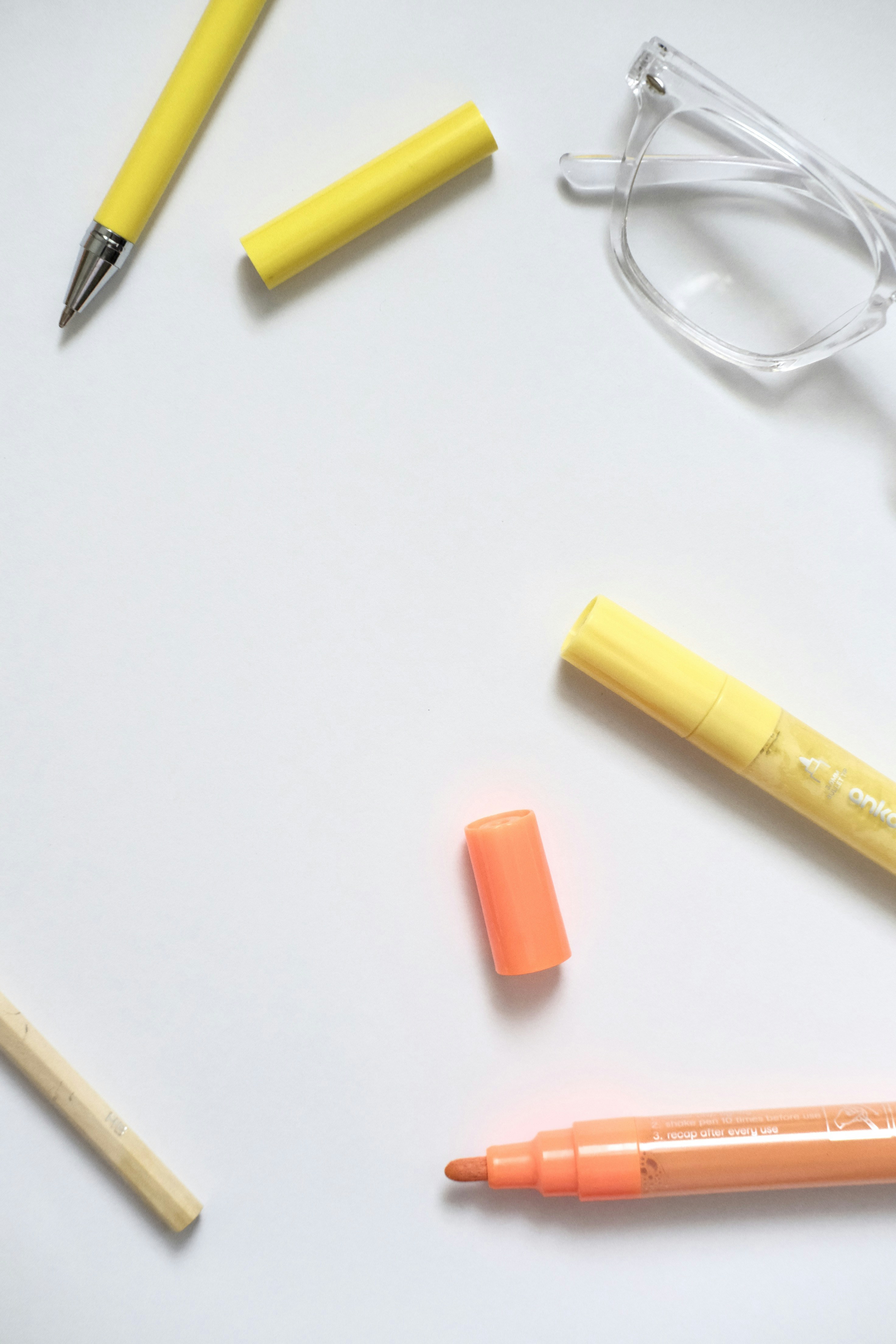 Yellow pen, highlighter, and glasses on white surface.
