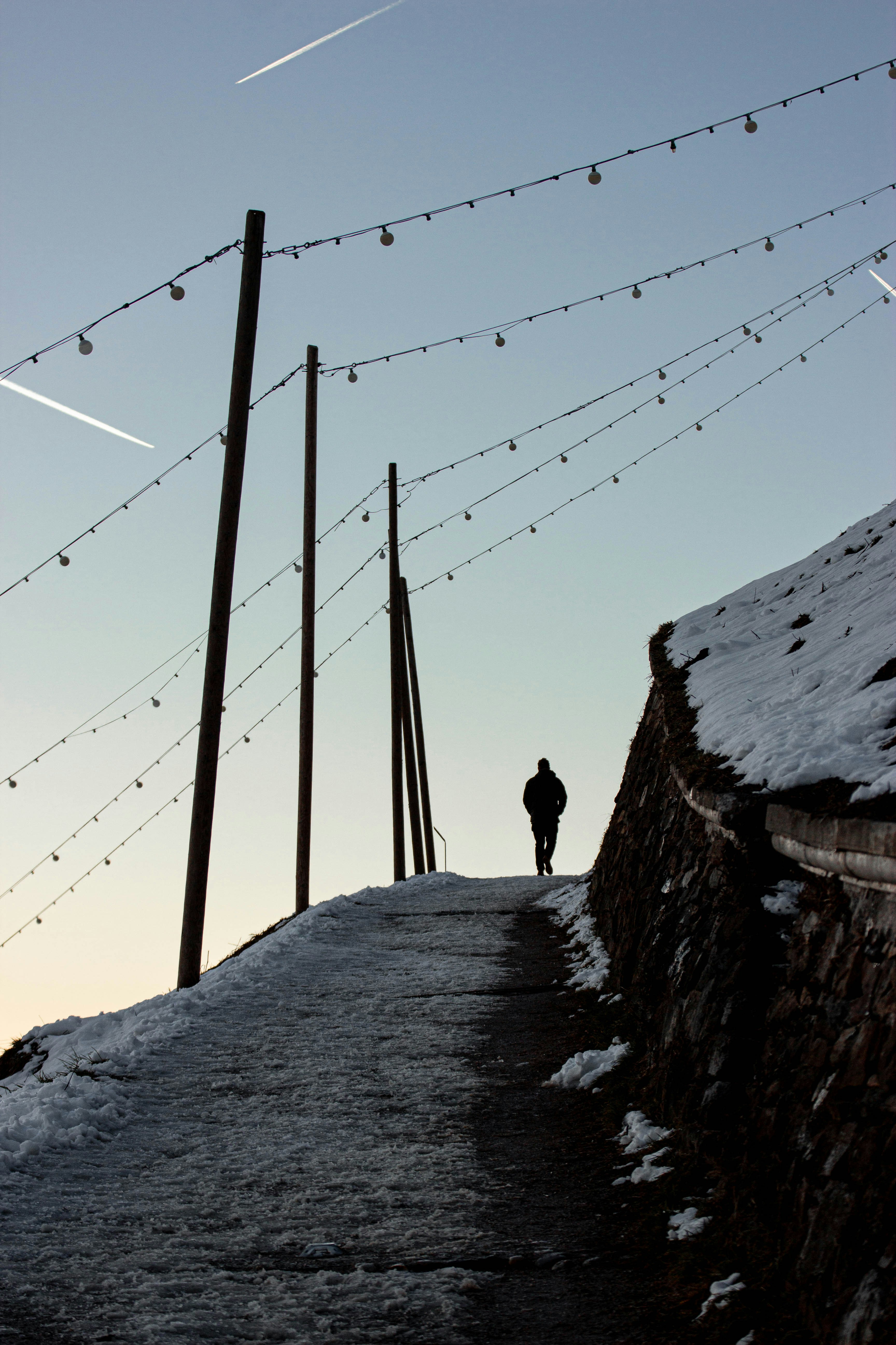 A lone figure walks up a snowy path with lights.