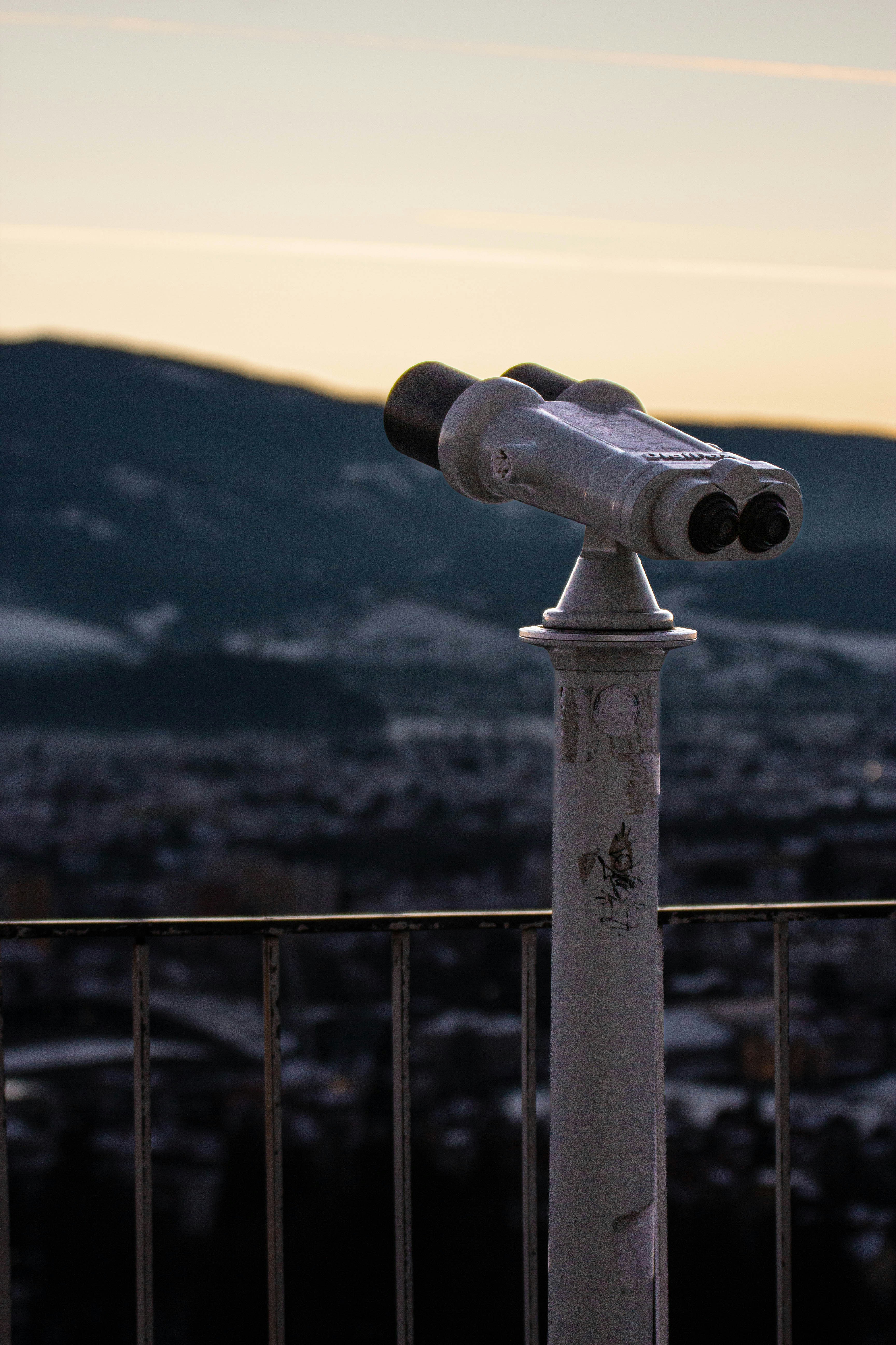 Binoculars overlook a snowy town at dusk.