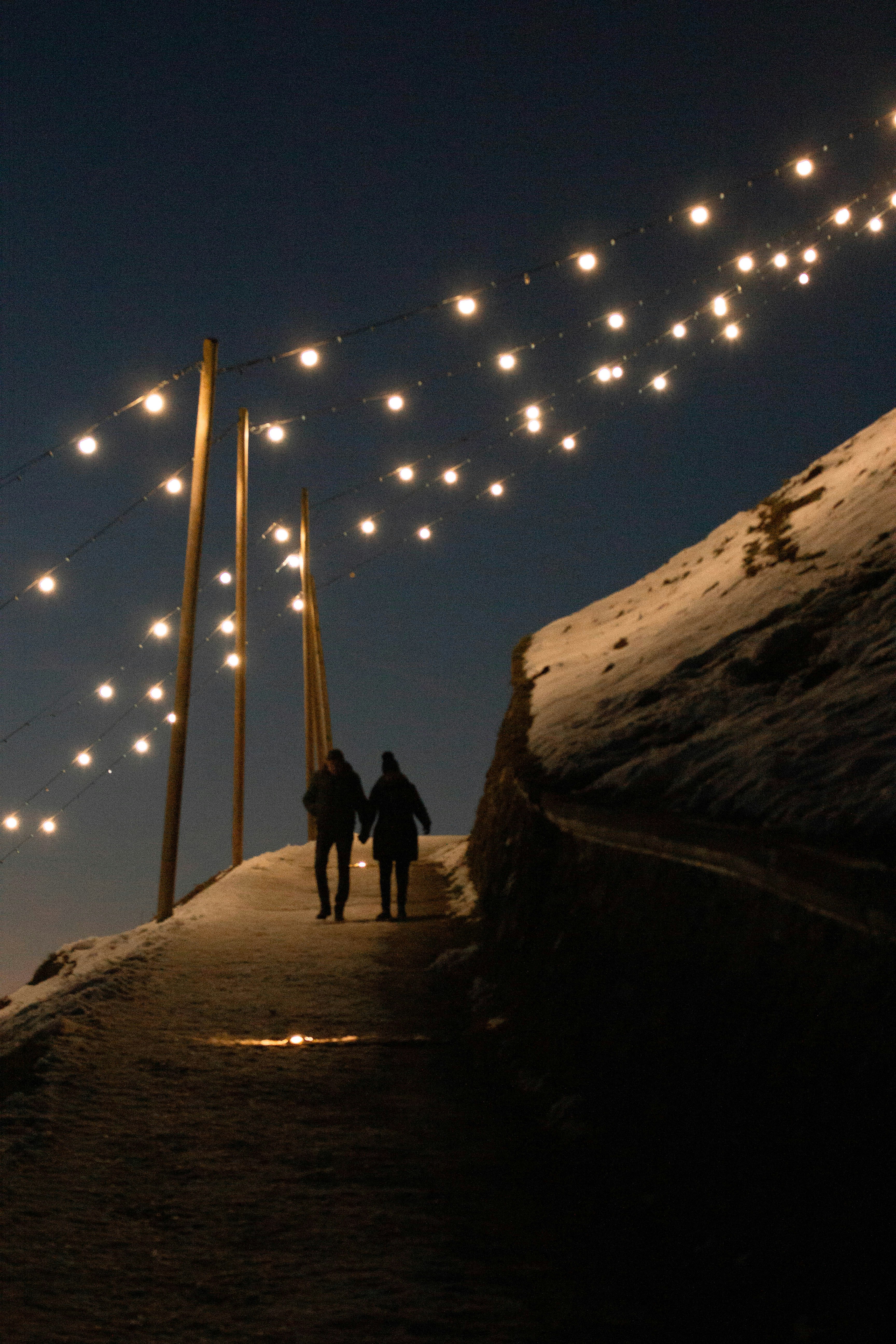 Couple walking on snowy path with string lights