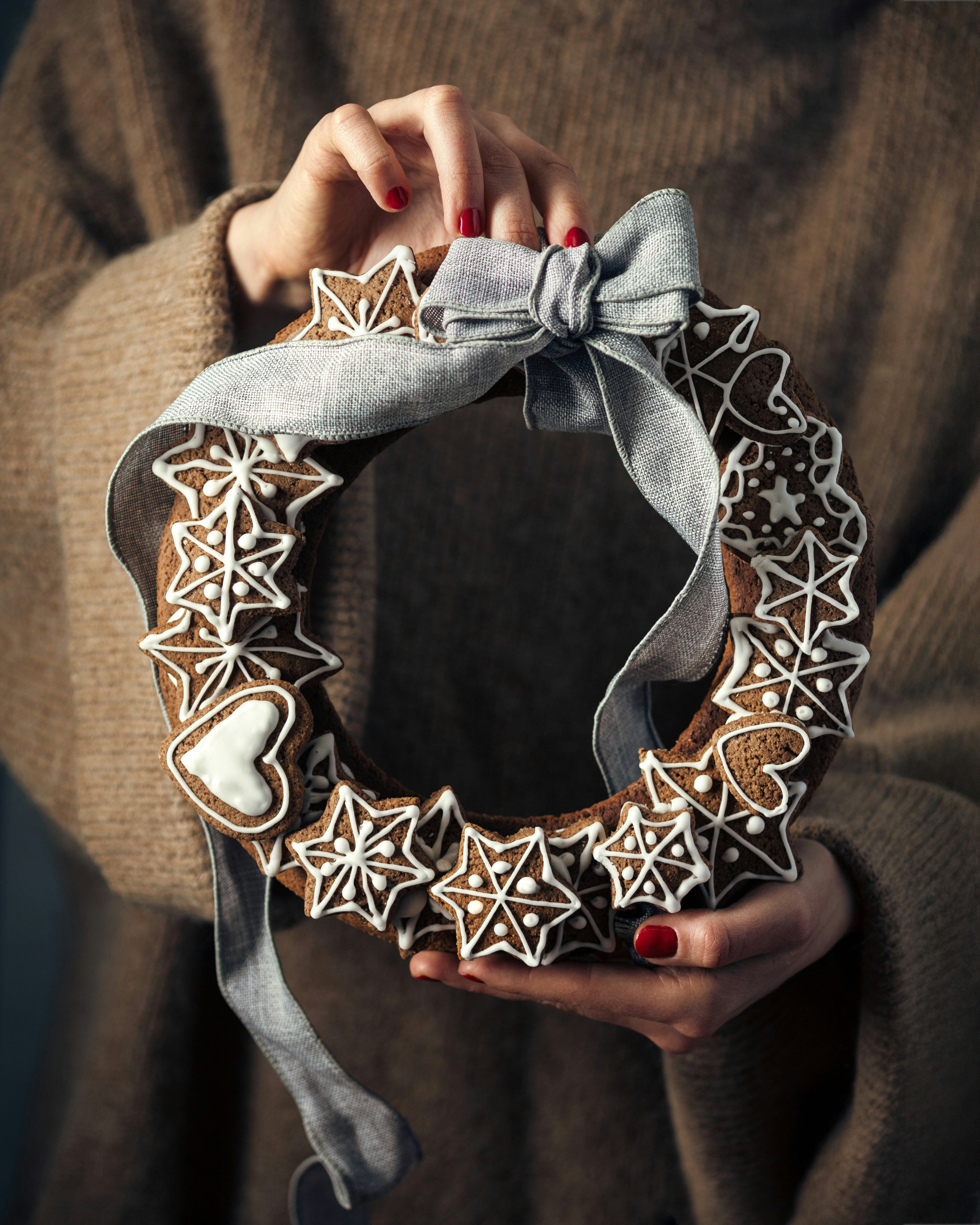 Person holding a gingerbread cookie wreath with ribbon