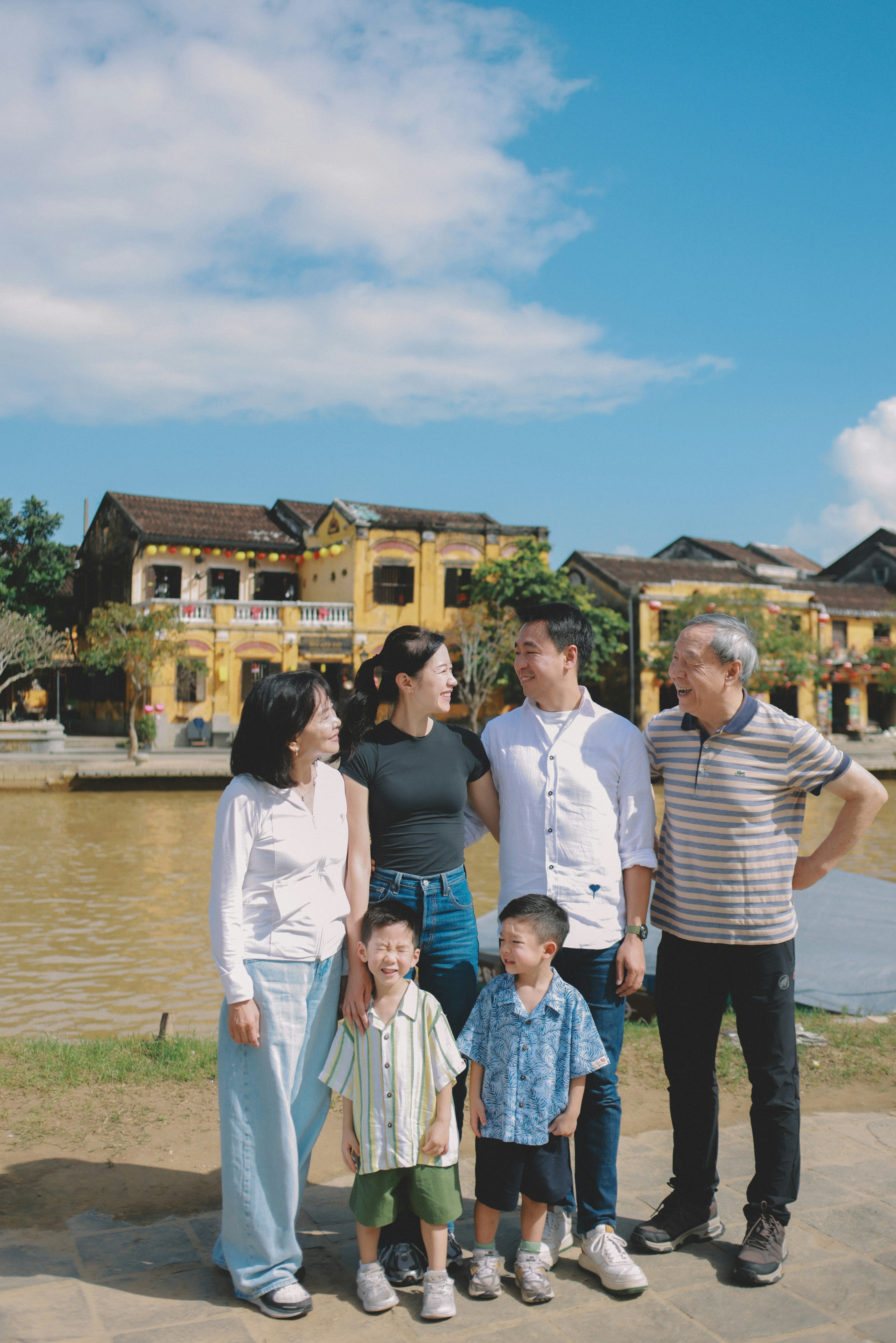 A multi-generational family poses outdoors by a river.