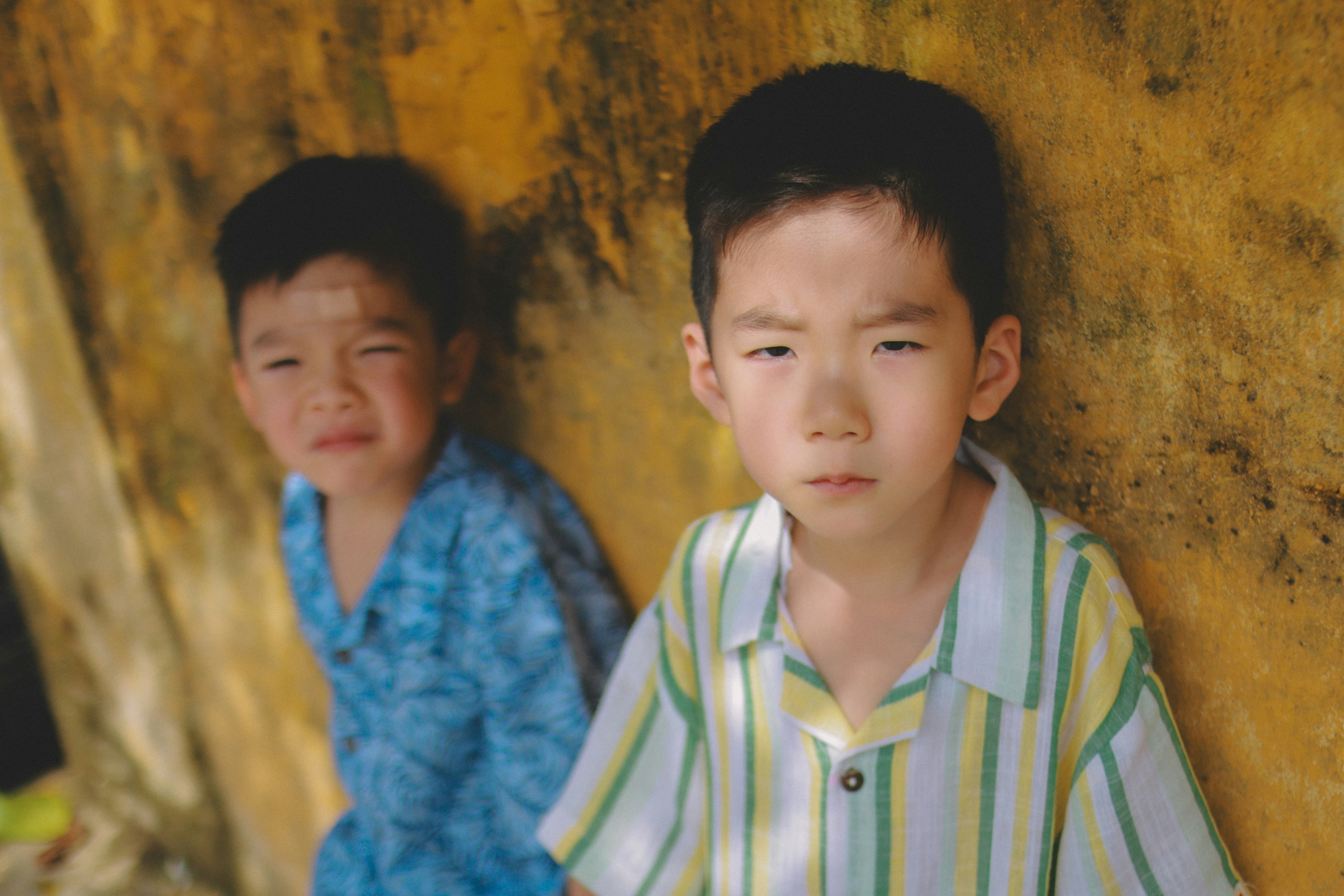 Two young boys stand against a textured wall.
