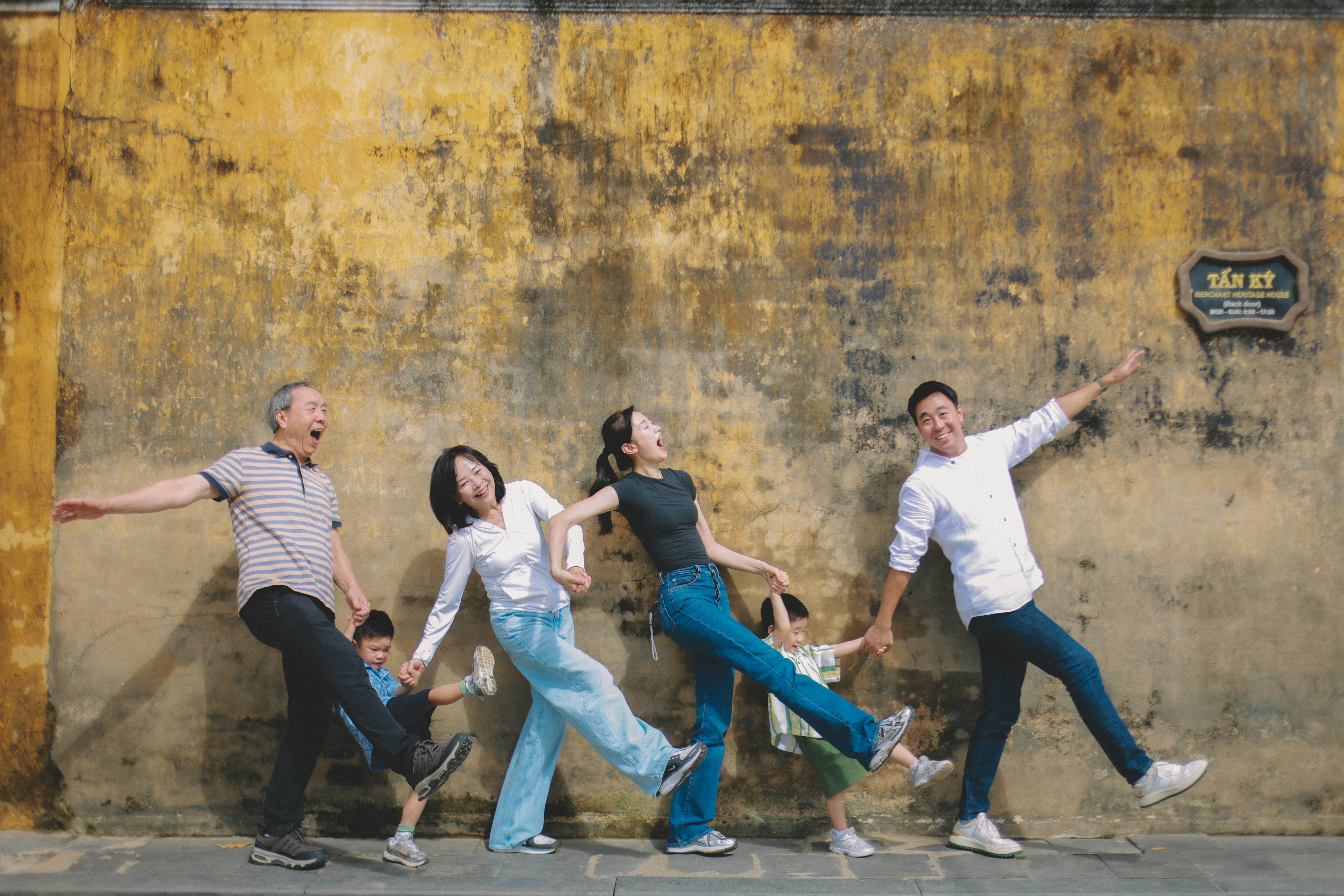 Famiglia che posa giocosamente contro una parete gialla testurizzata.