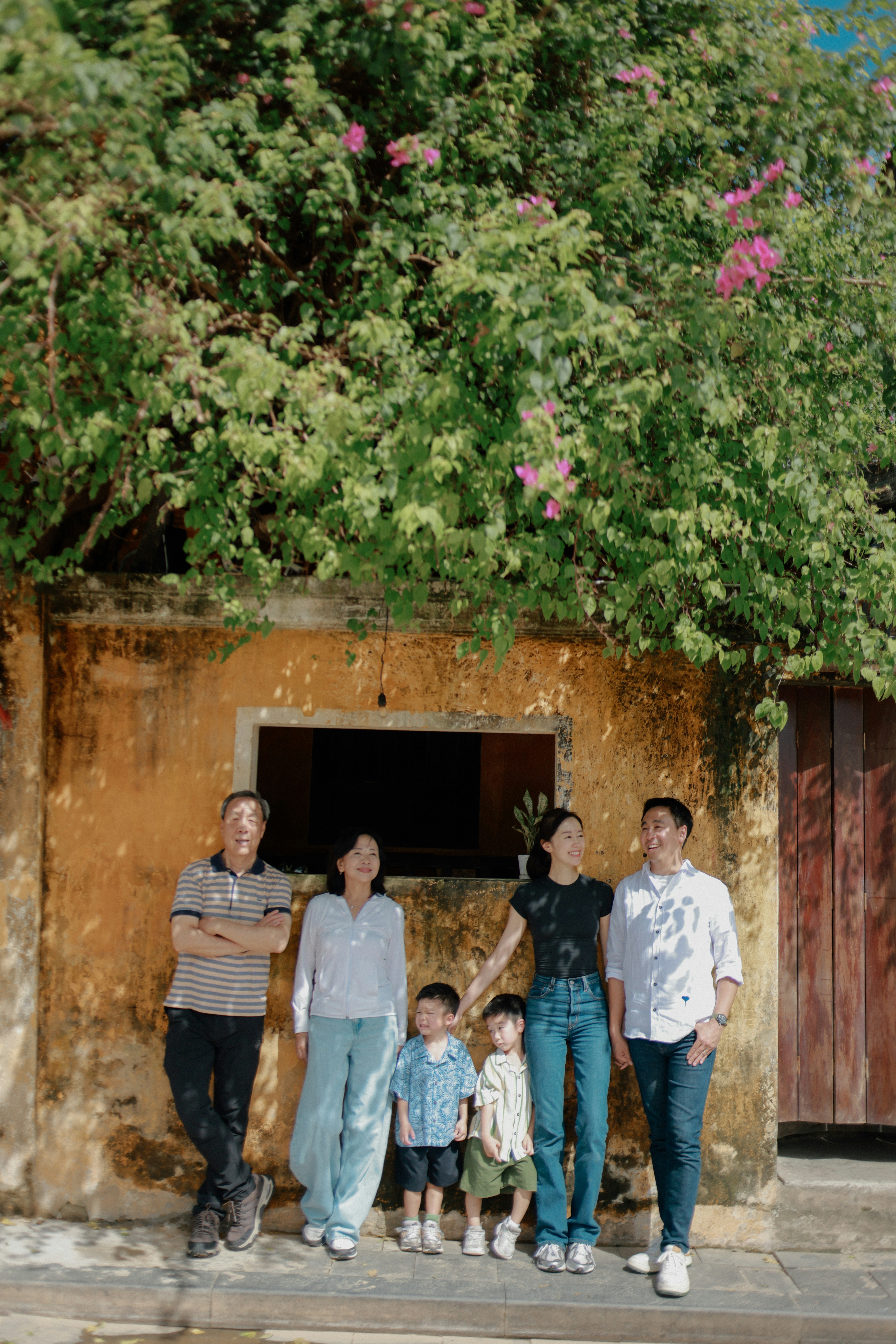 Family posing against a weathered wall under greenery.