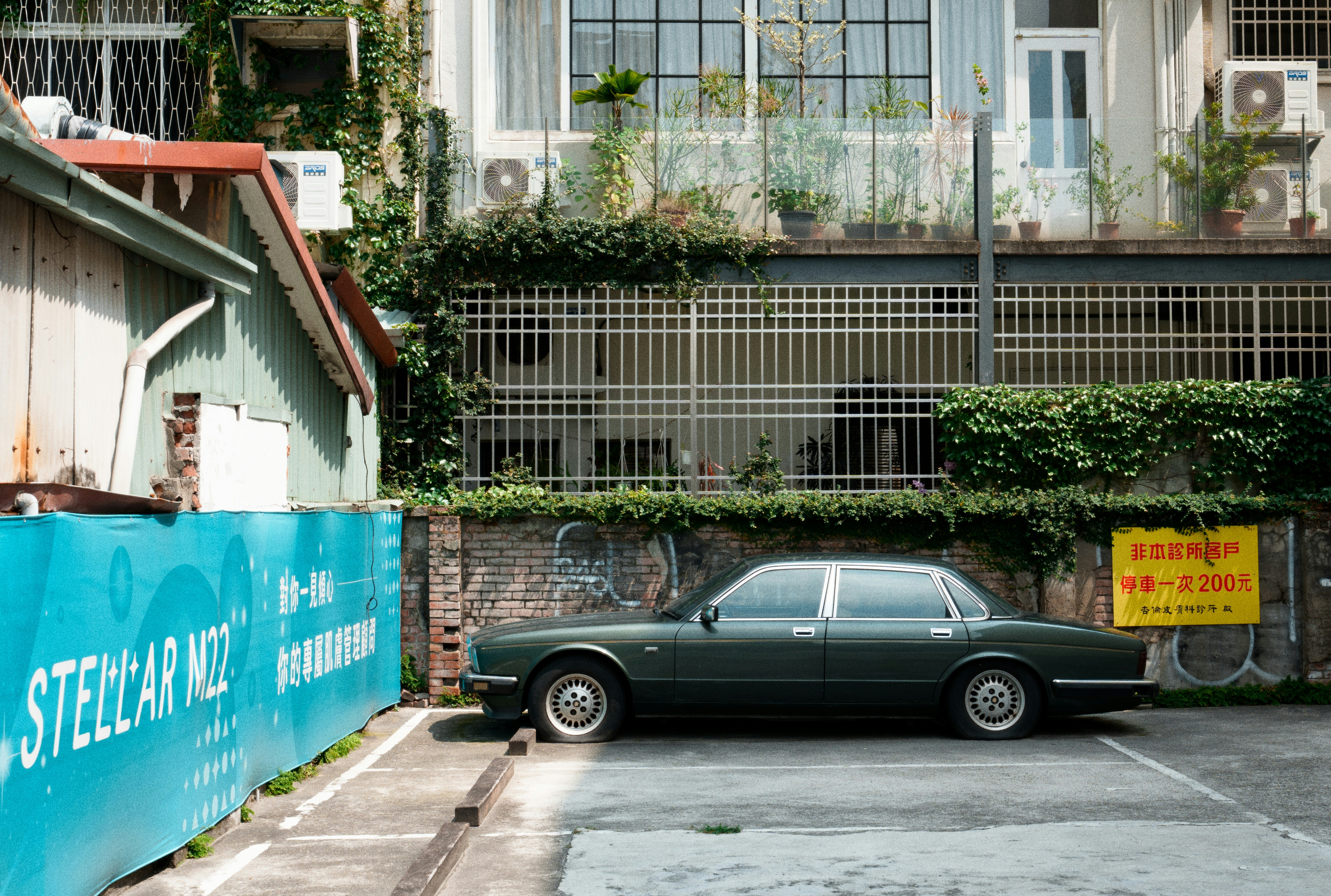 Dark green vintage car parked near a teal wall.