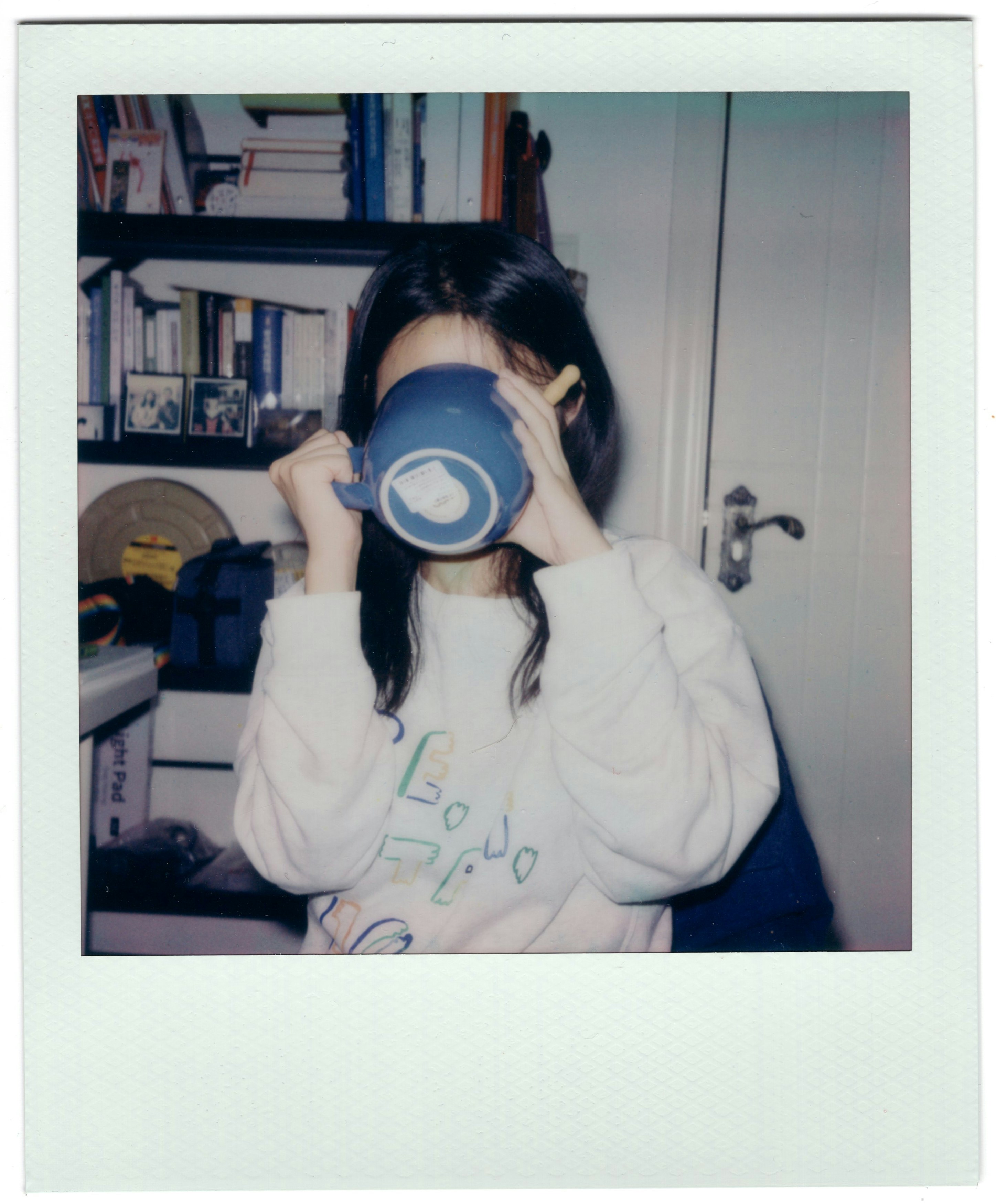 Woman drinking from a blue mug in front of bookshelf