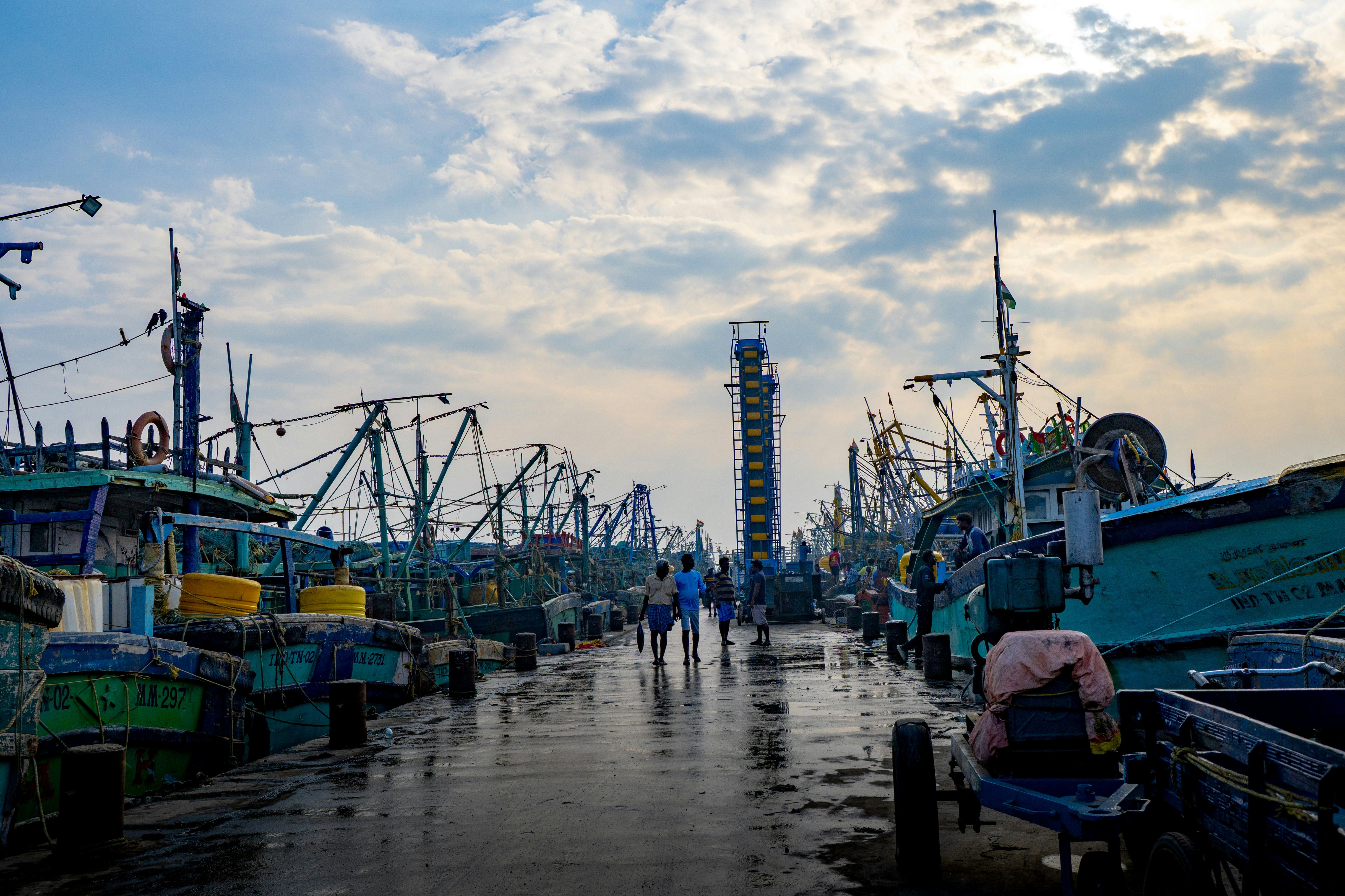 Fishing boats docked at a pier under a cloudy sky.
