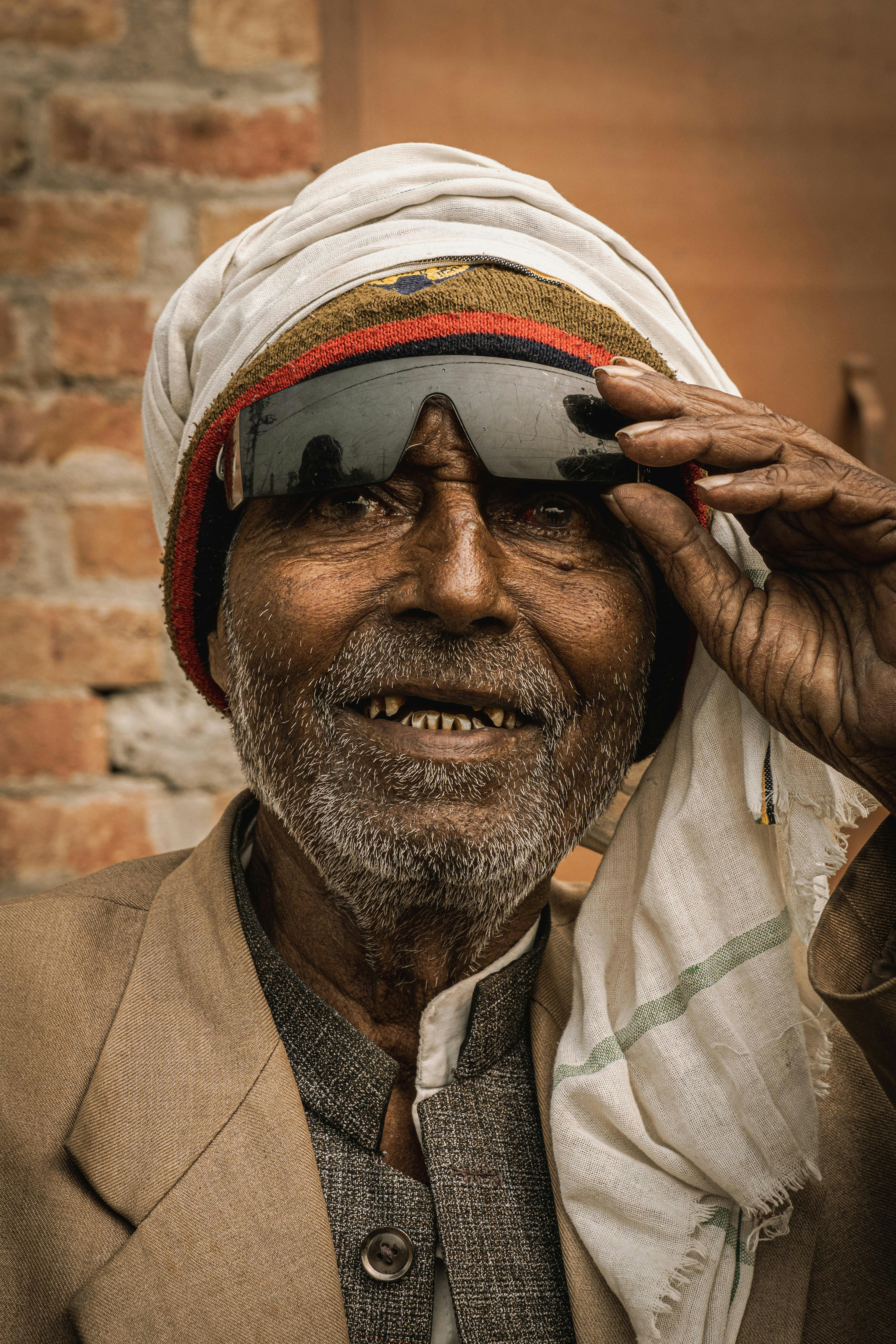 Elderly man with sunglasses and head wrap smiles.