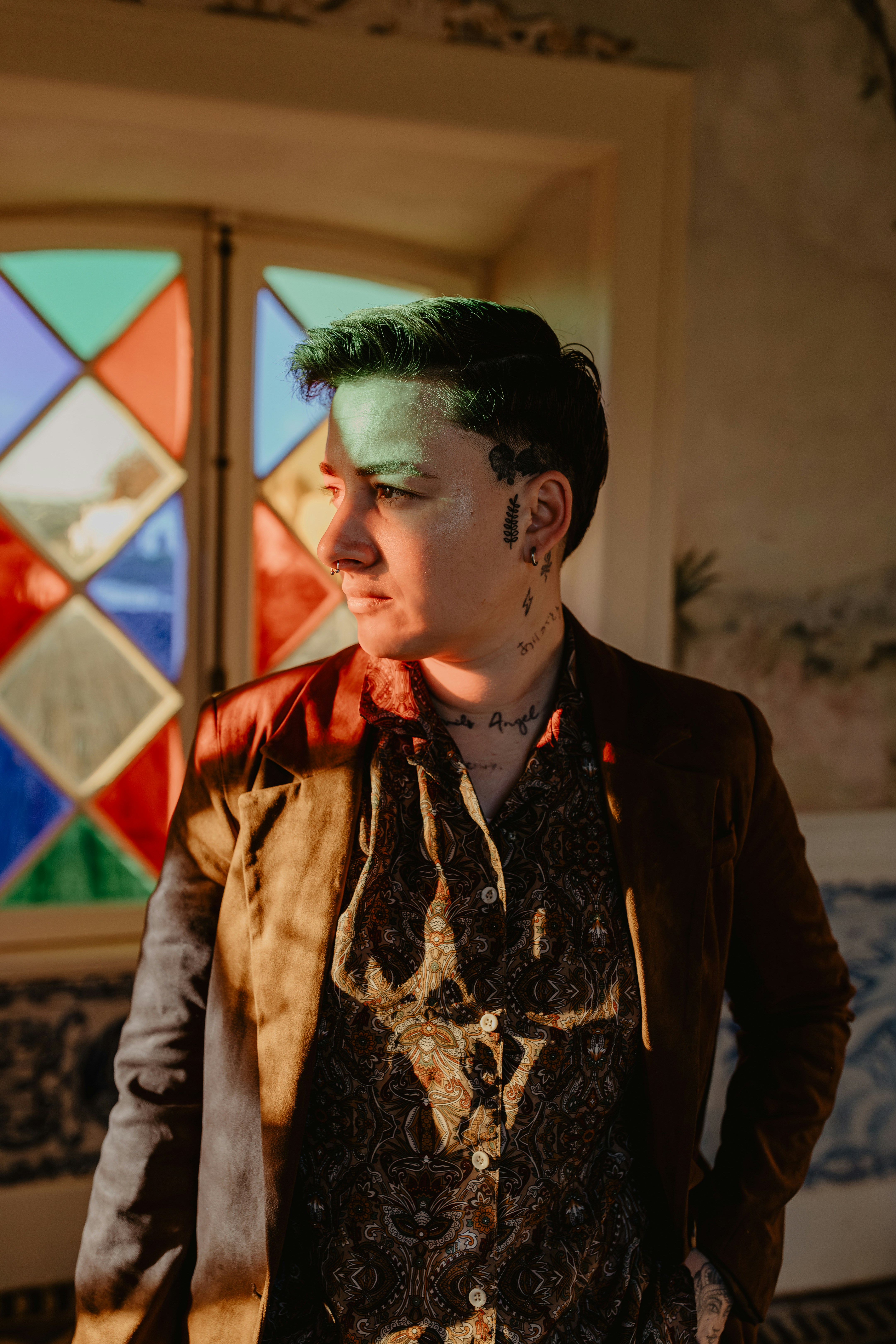 Man in patterned shirt and jacket near stained glass.