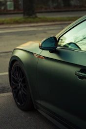 Matte dark green car parked on asphalt street.