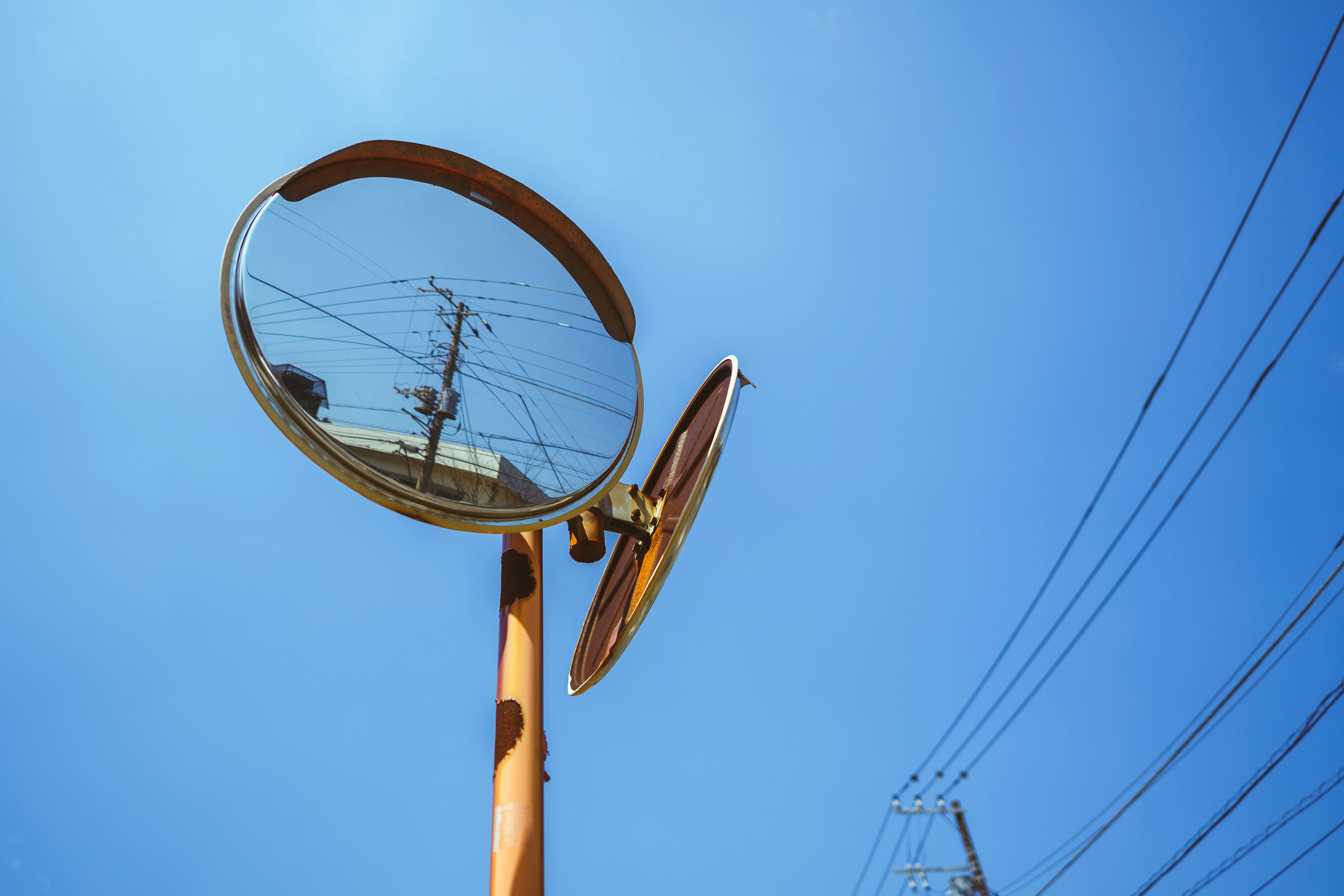 Convex mirror reflecting buildings and wires against sky
