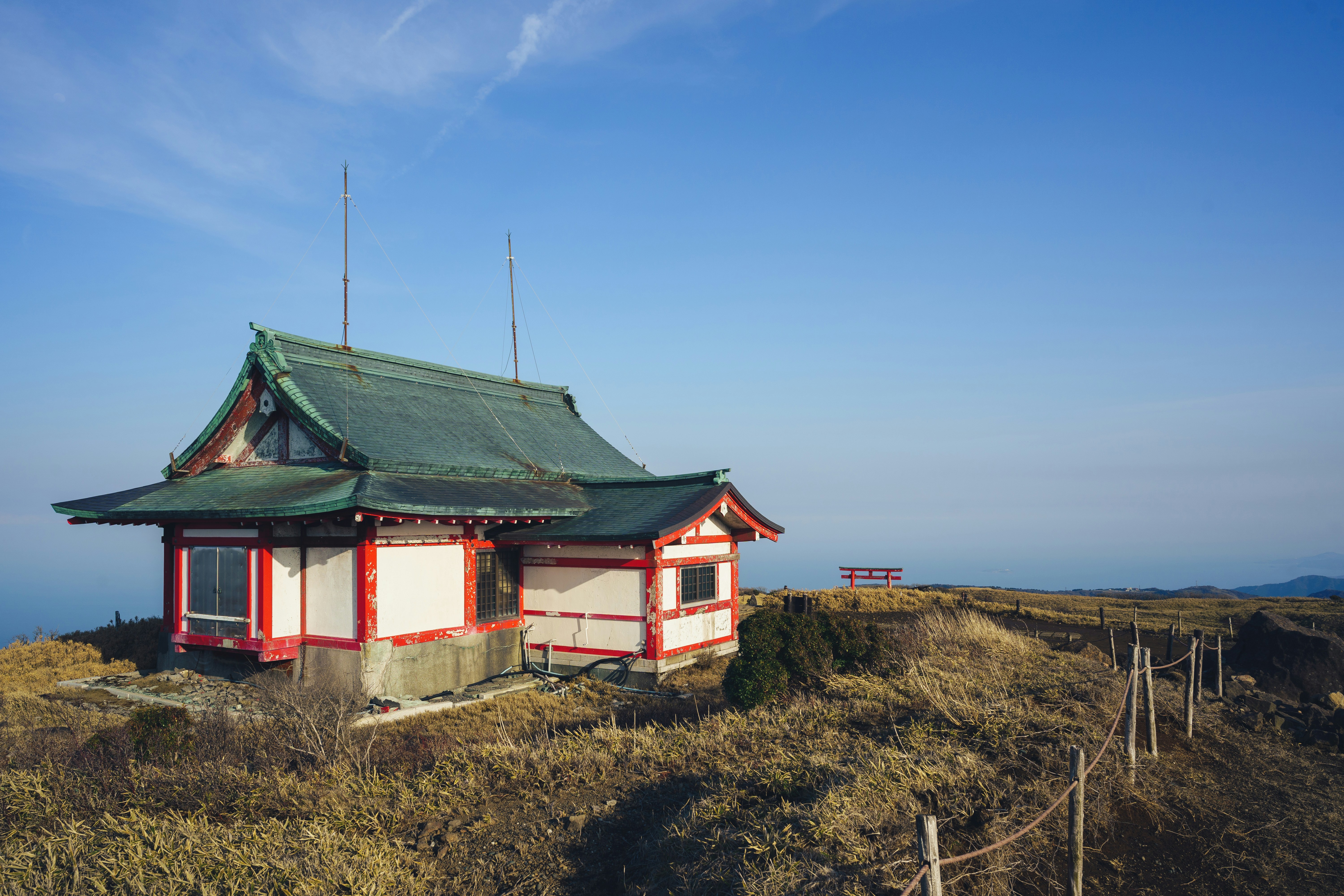 Small japanese shrine on a grassy hilltop under blue sky