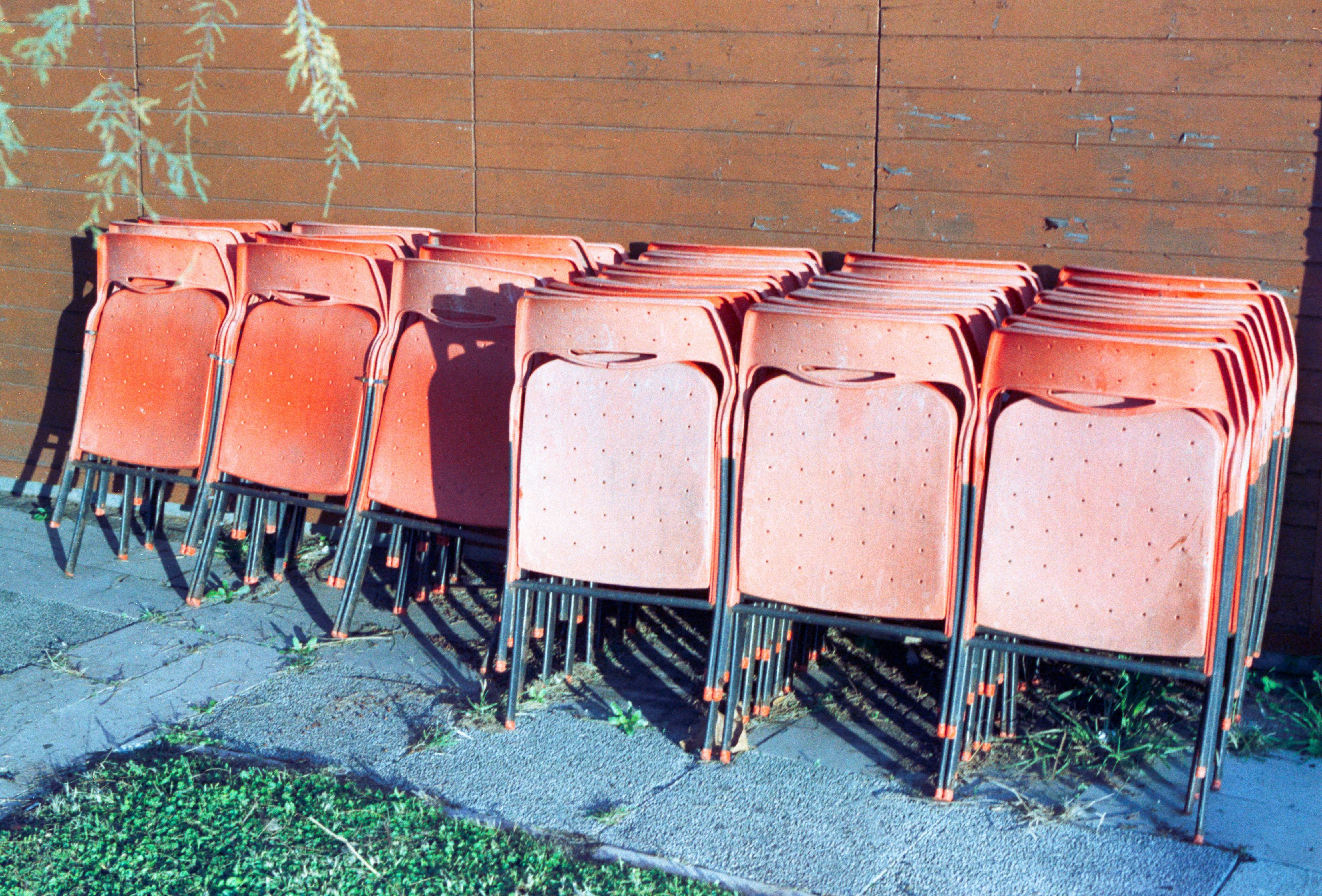Stacked orange plastic chairs against a wooden wall.