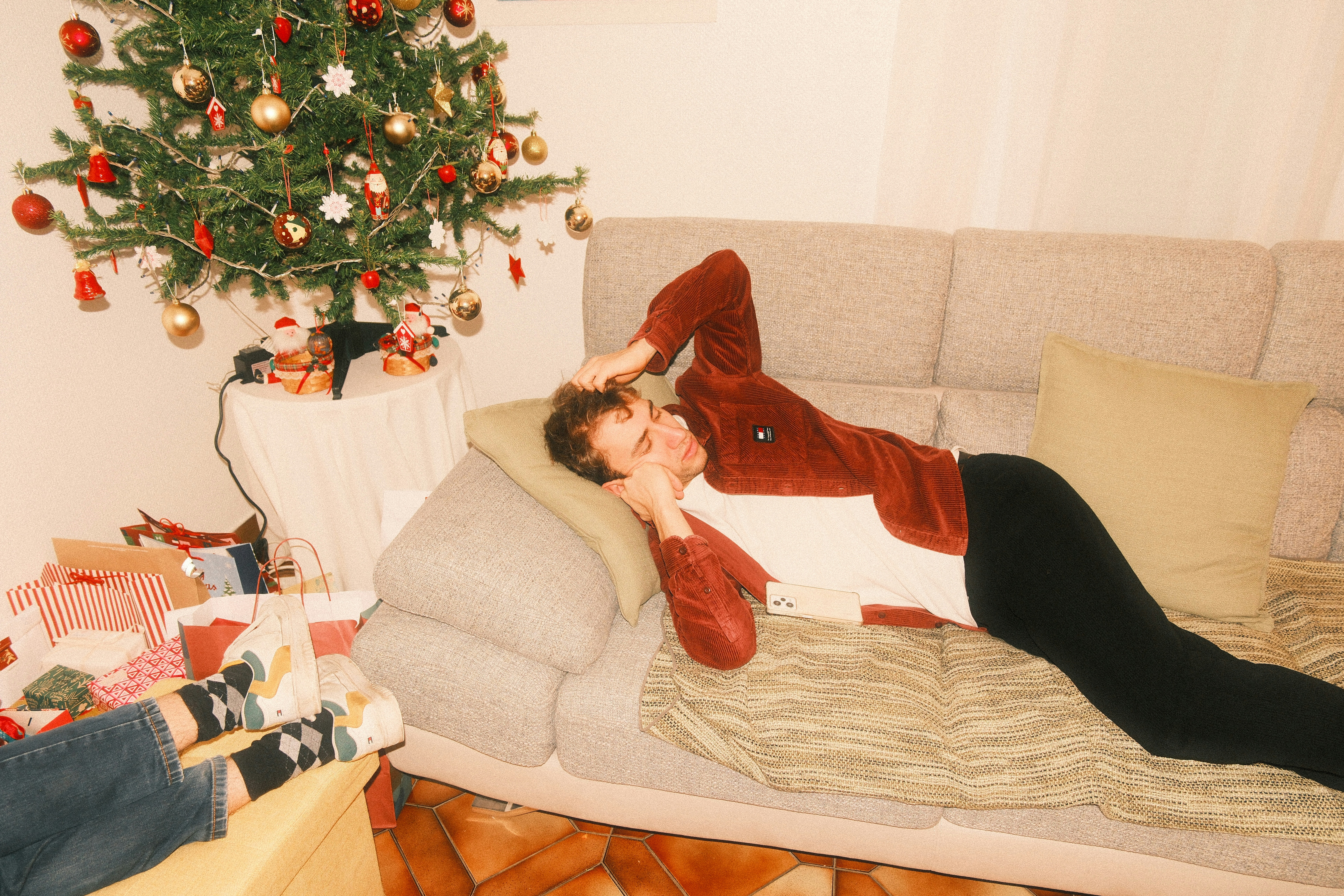 A person relaxes on a couch near a christmas tree.