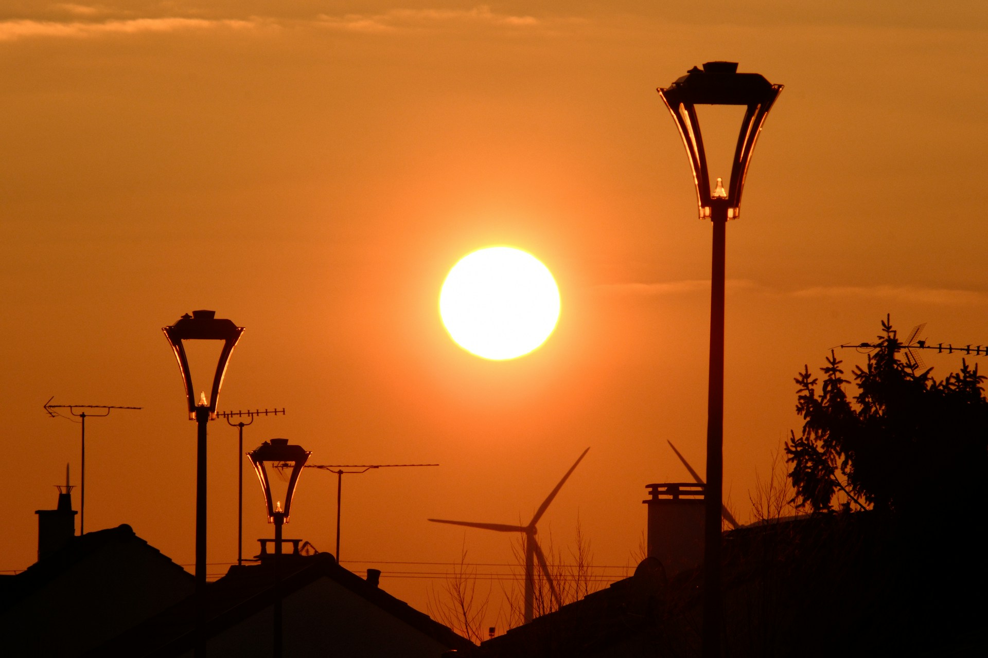 Sunset over rooftops with streetlights and wind turbine.