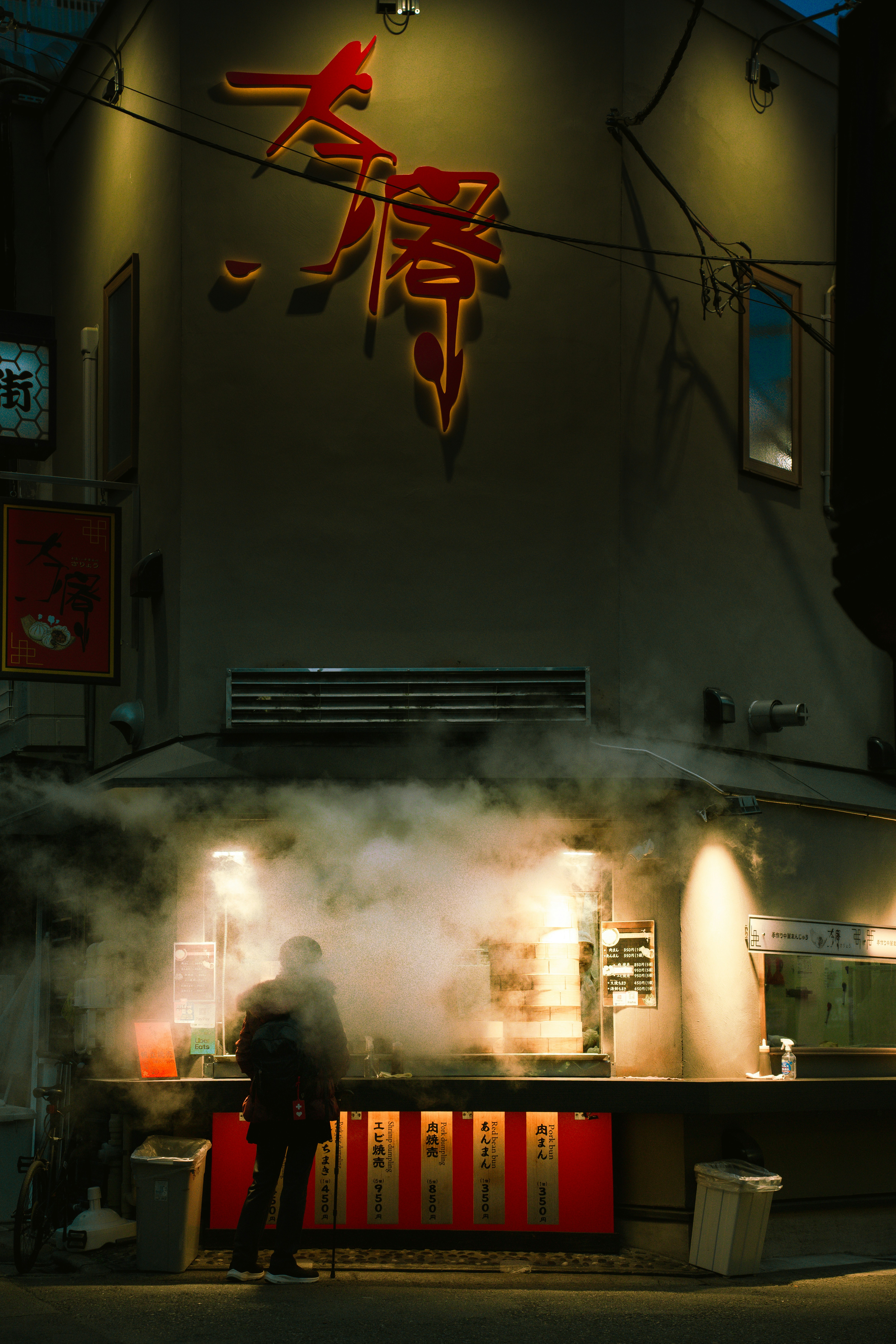 Person standing at a steamy food stall at night.