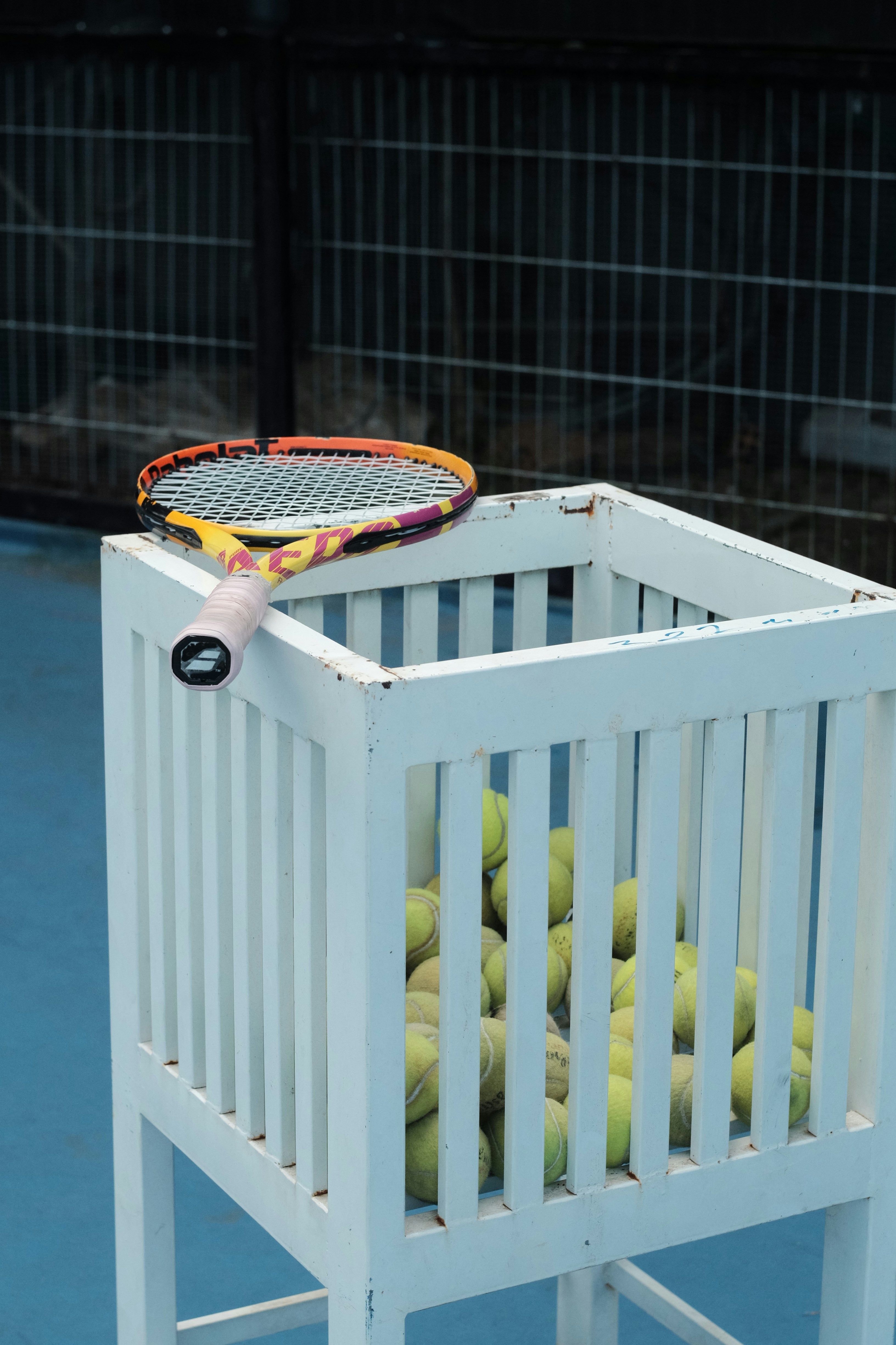 Raquette de tennis et balles dans un panier en bois blanc.