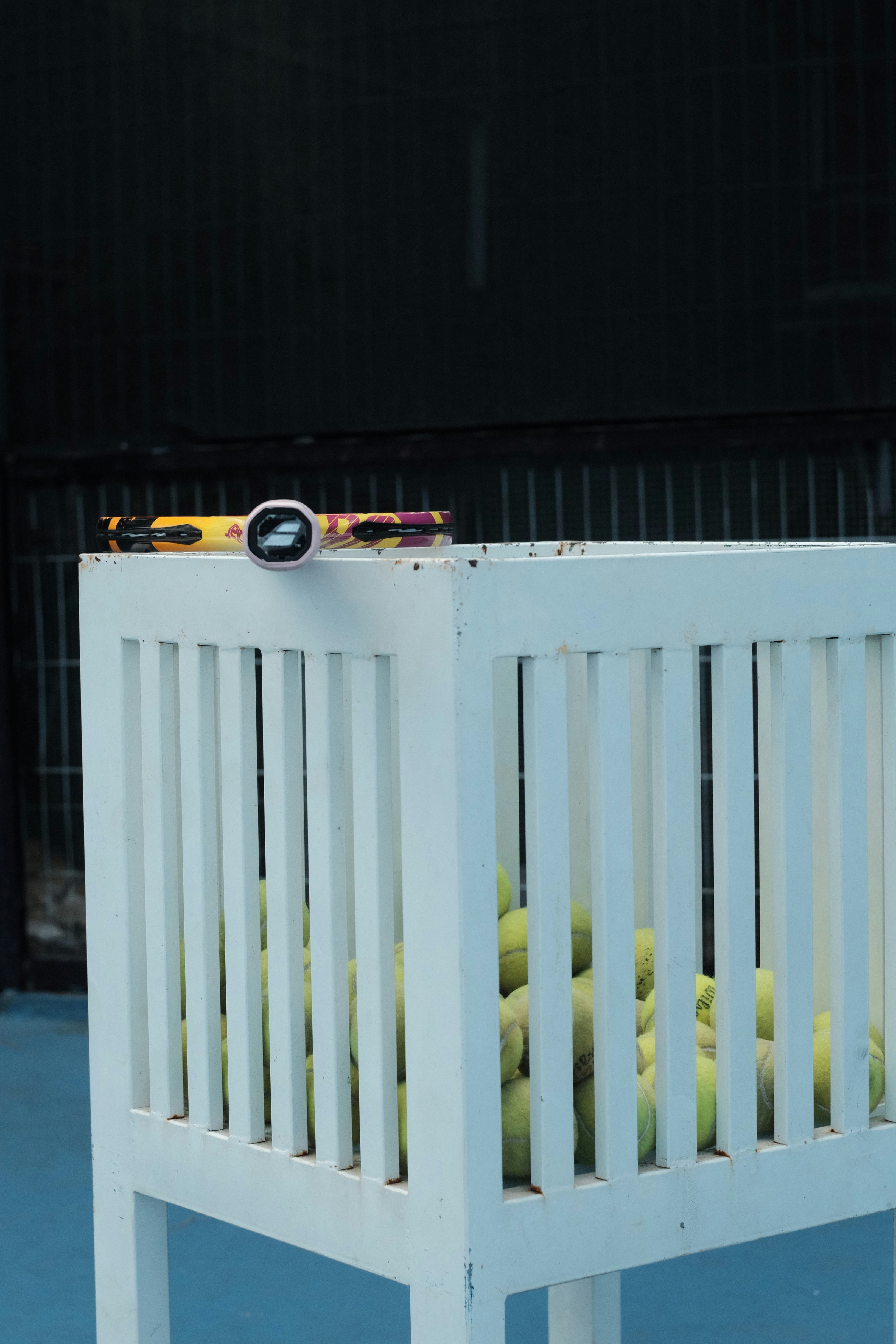 White basket filled with tennis balls on blue court