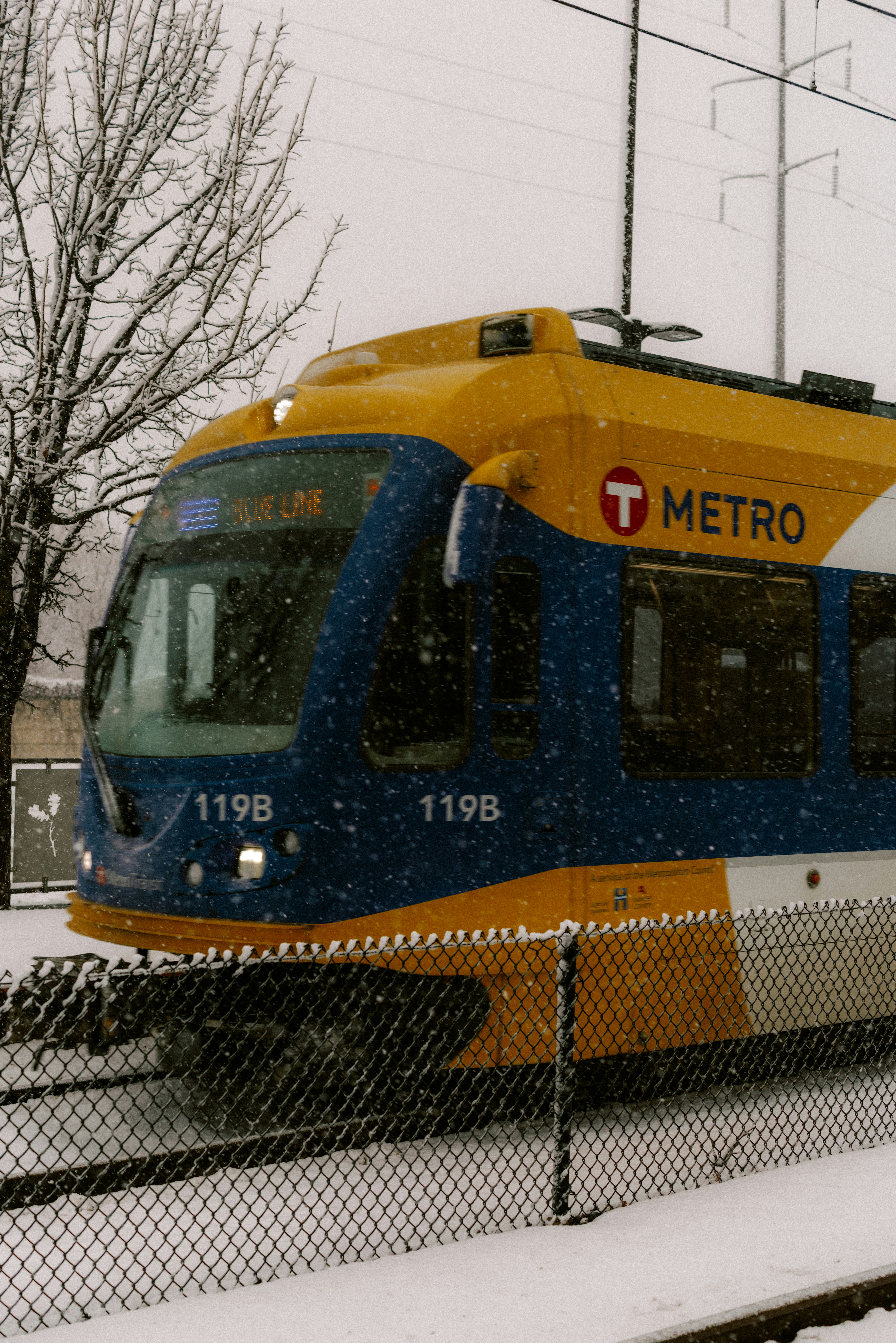 A blue and yellow metro train in the snow.