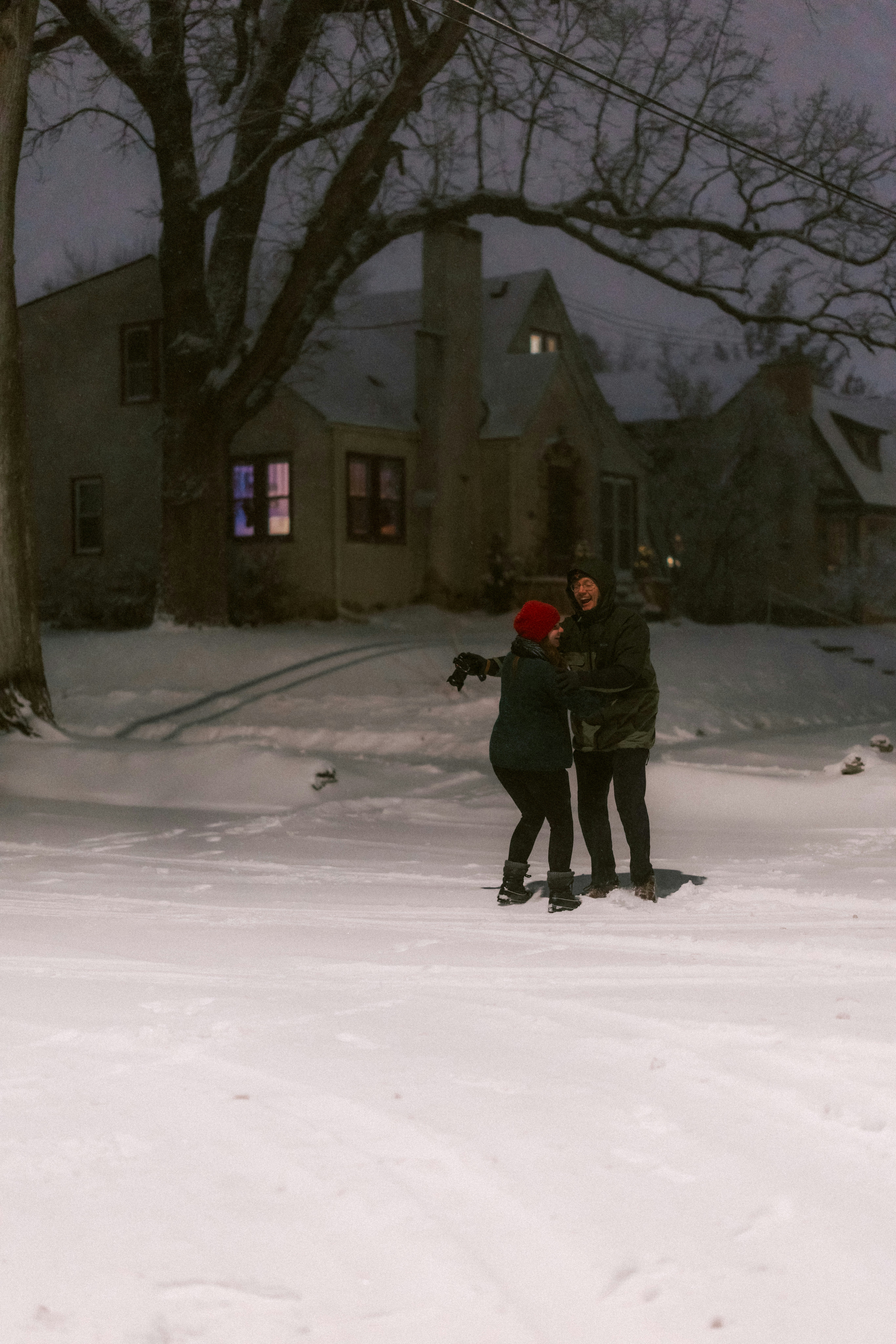 Couple embracing in snowy yard at dusk