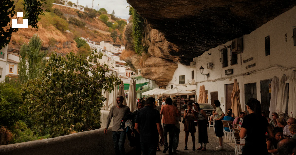 Saliente Rocoso La gente camina bajo un saliente rocoso en un pueblo blanco. foto ...