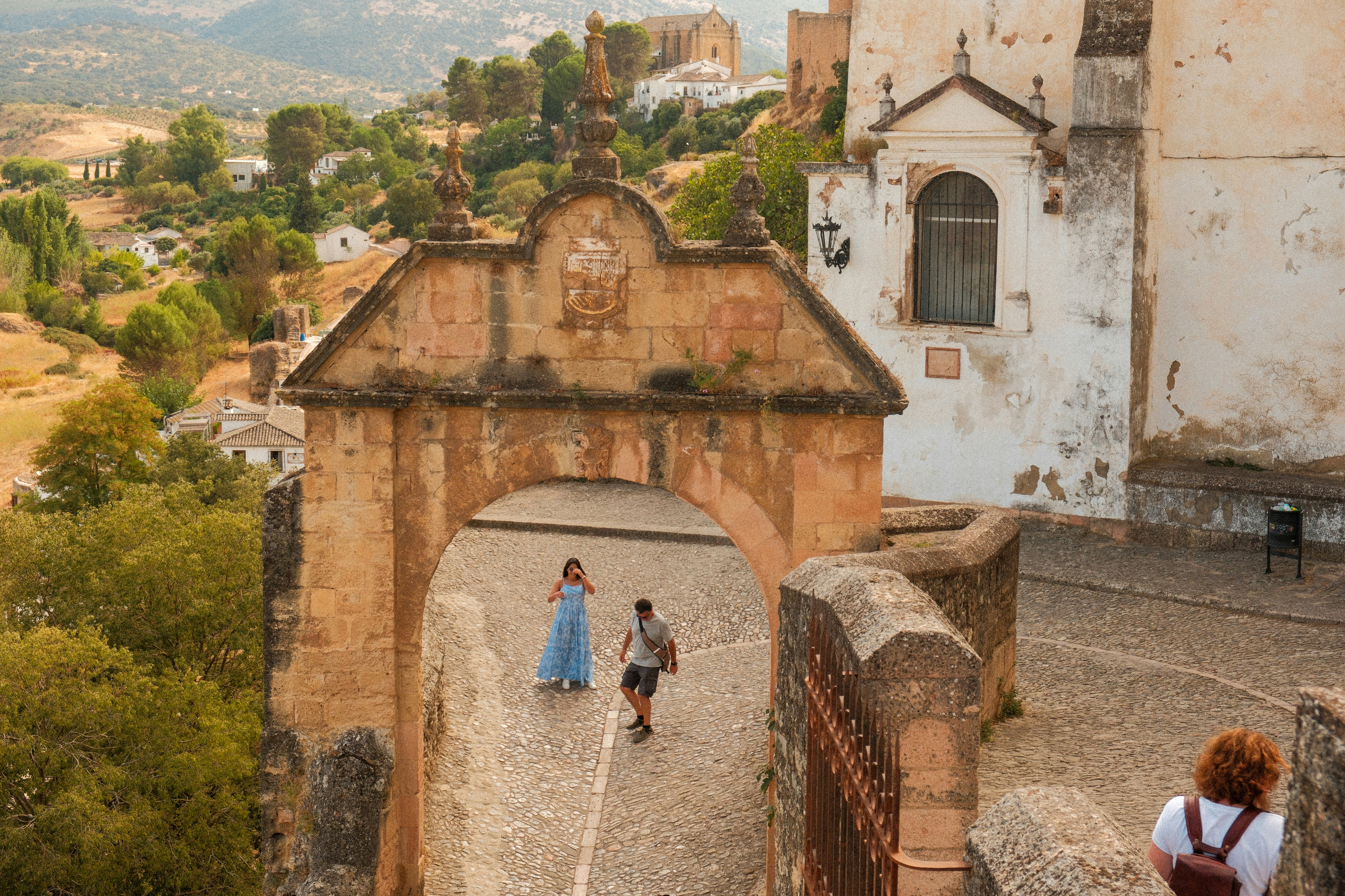 Couple walks through ancient stone archway in historic town.