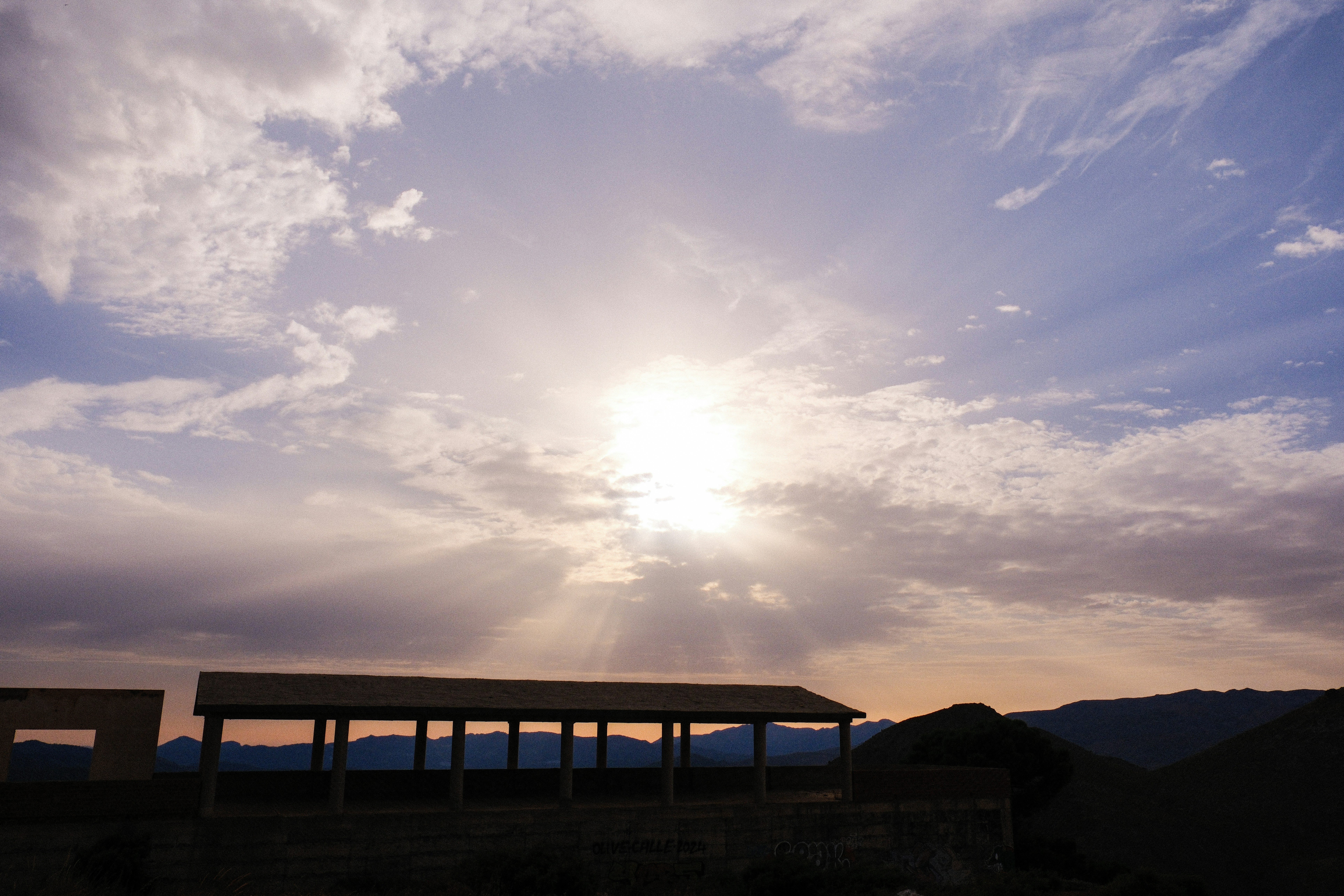 Sunbeams breaking through clouds over a structure.