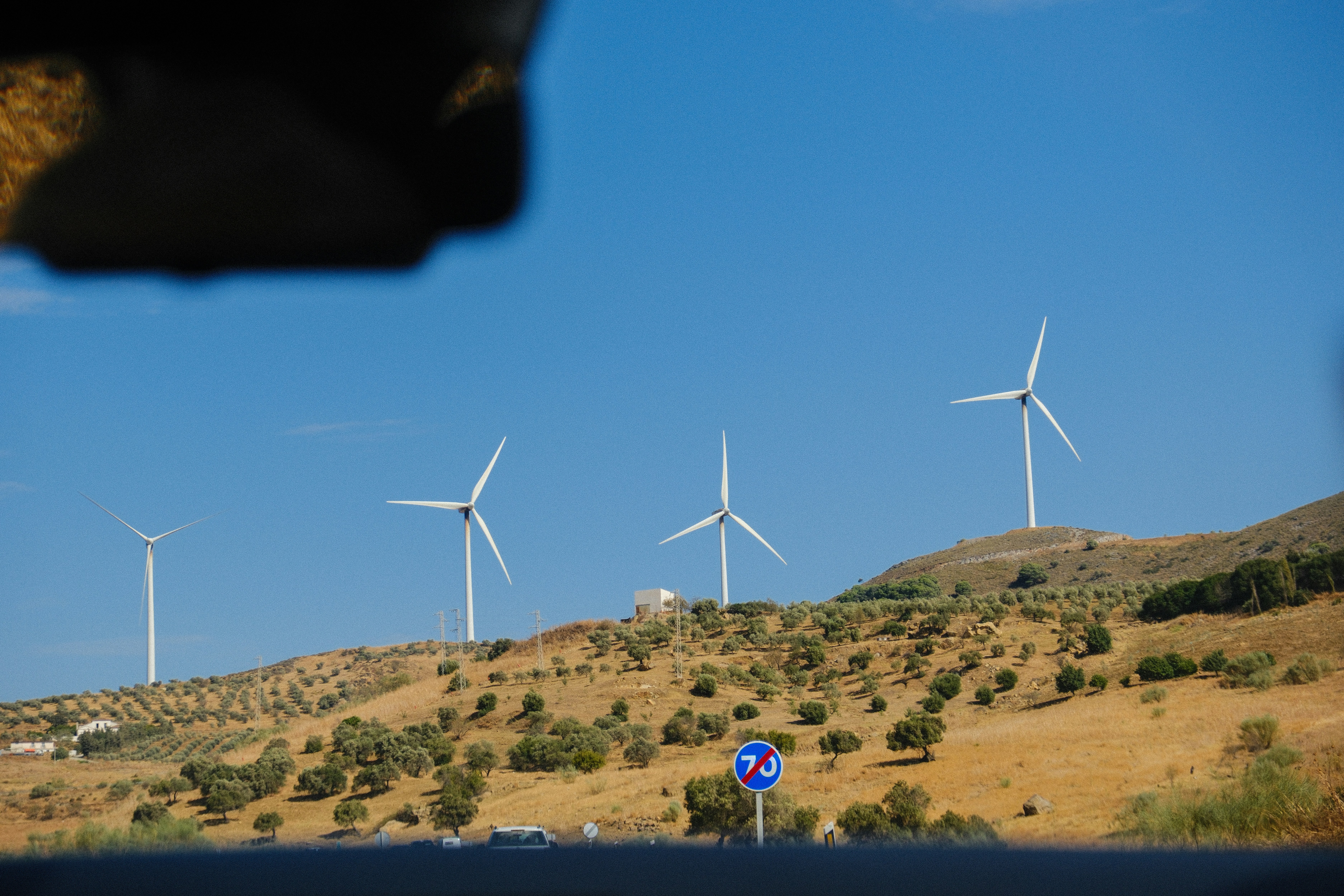 Wind turbines on a grassy hill under blue sky.