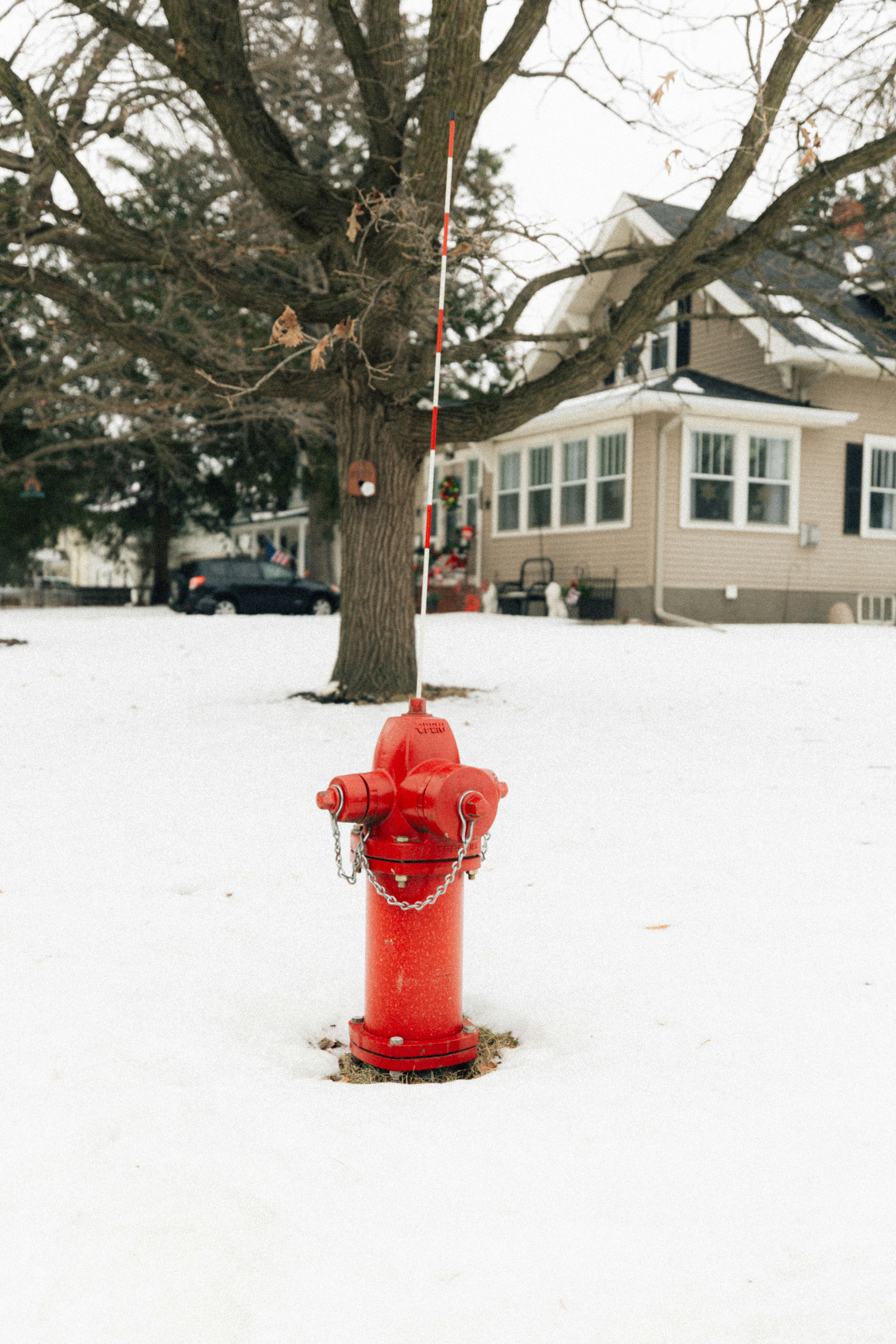 Red fire hydrant in snowy yard with house.