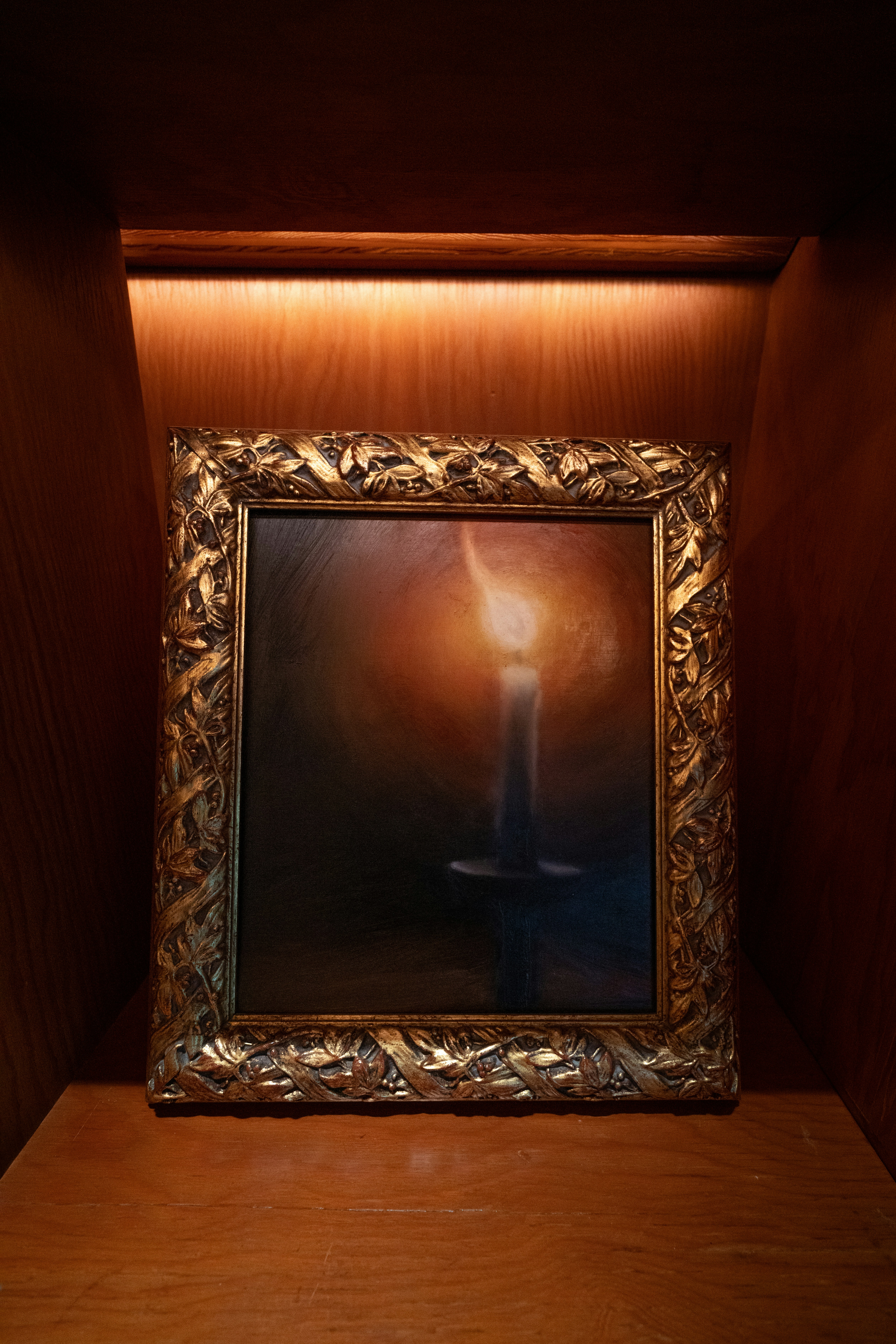 A painting of a lit candle in a golden frame.