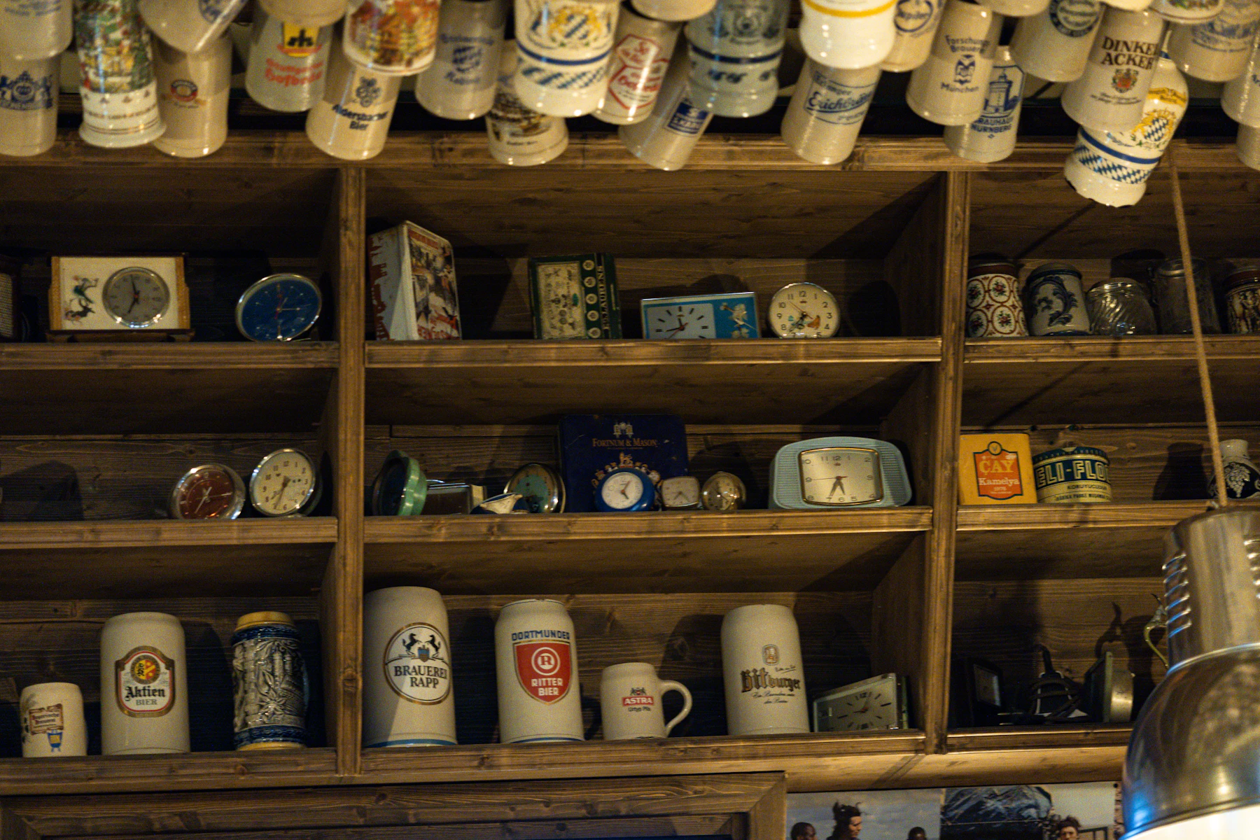 Wooden shelves holding stoneware beer steins and old clocks, with more steins hanging in a row above