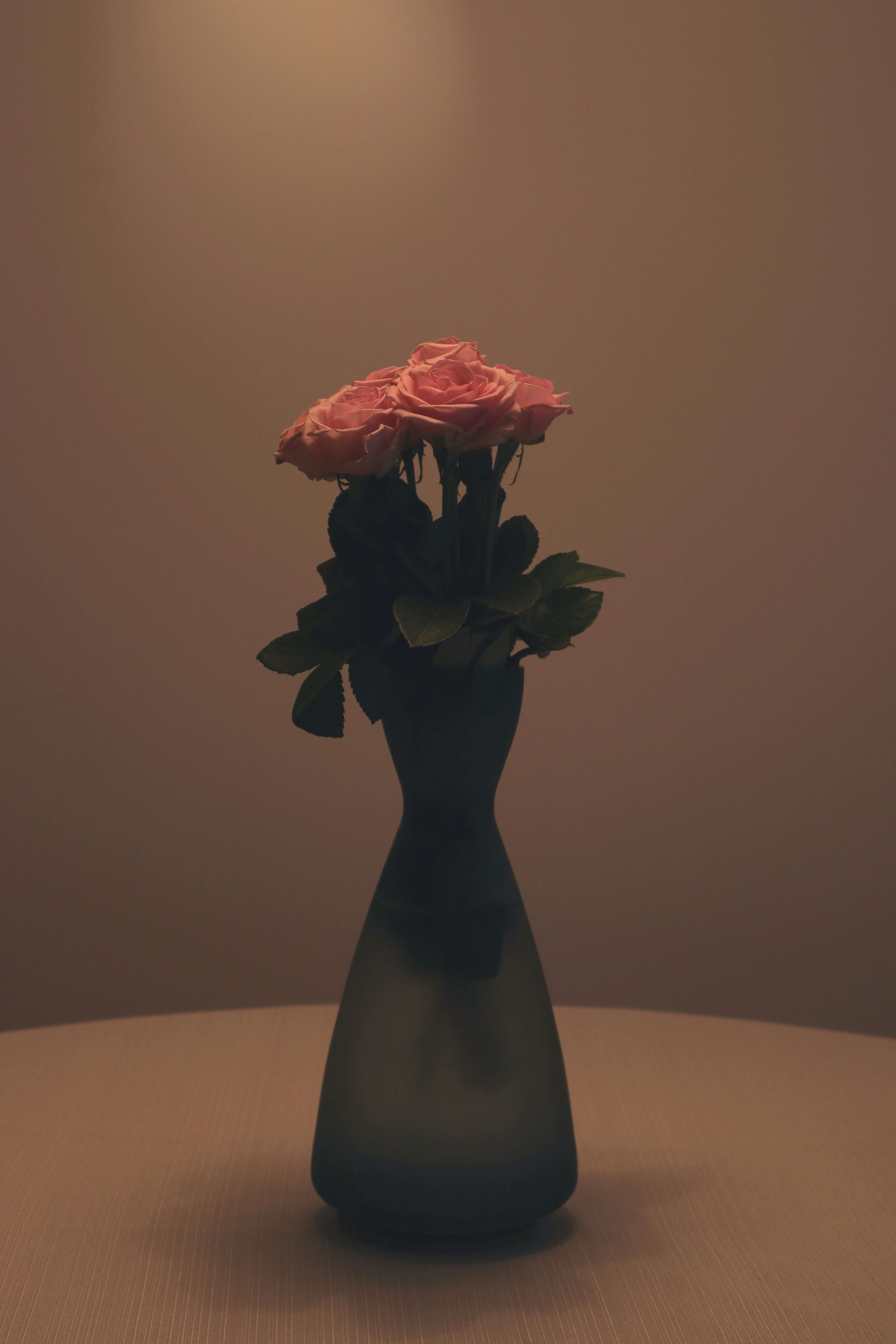 Pink roses in a dark vase on a table.
