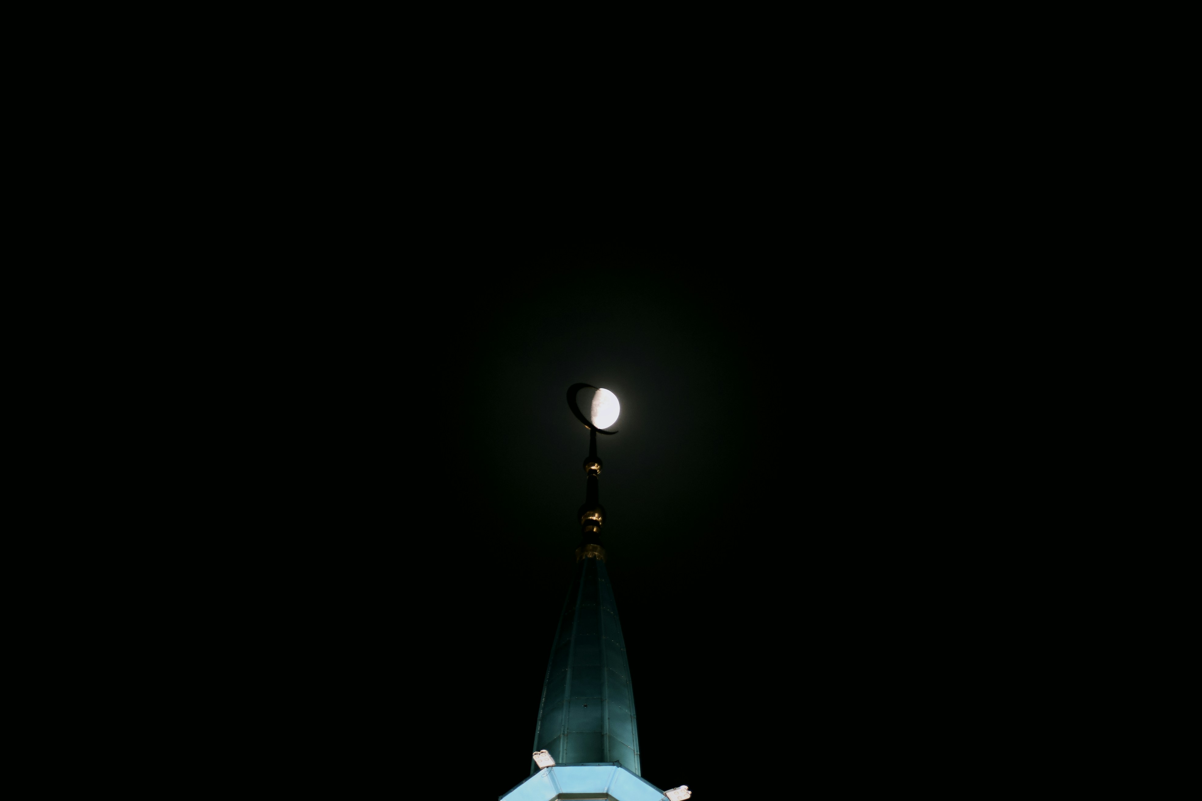 Half moon shining over a building spire at night