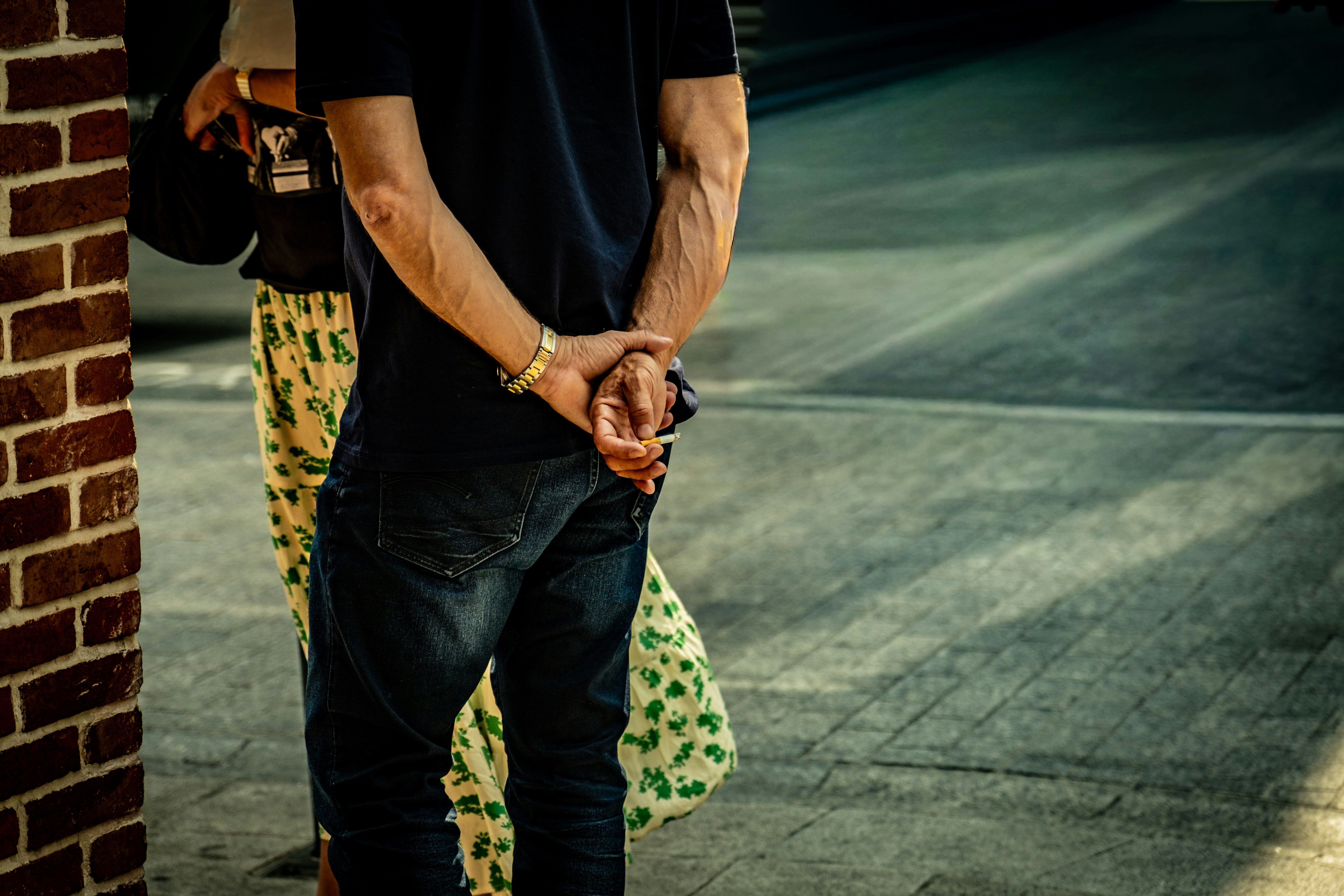 Two people stand near a brick wall outdoors.