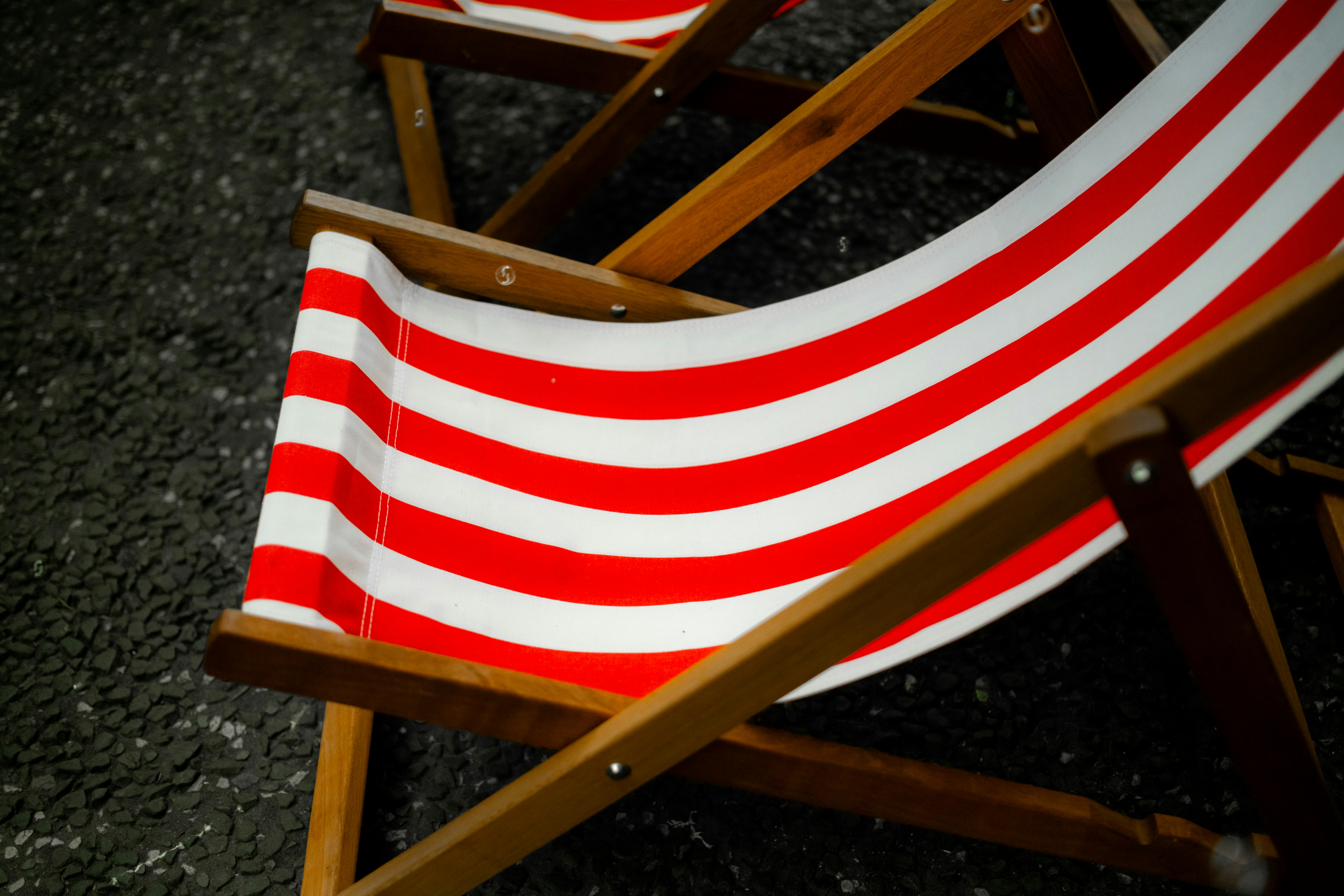 Two red and white striped deck chairs on pavement.