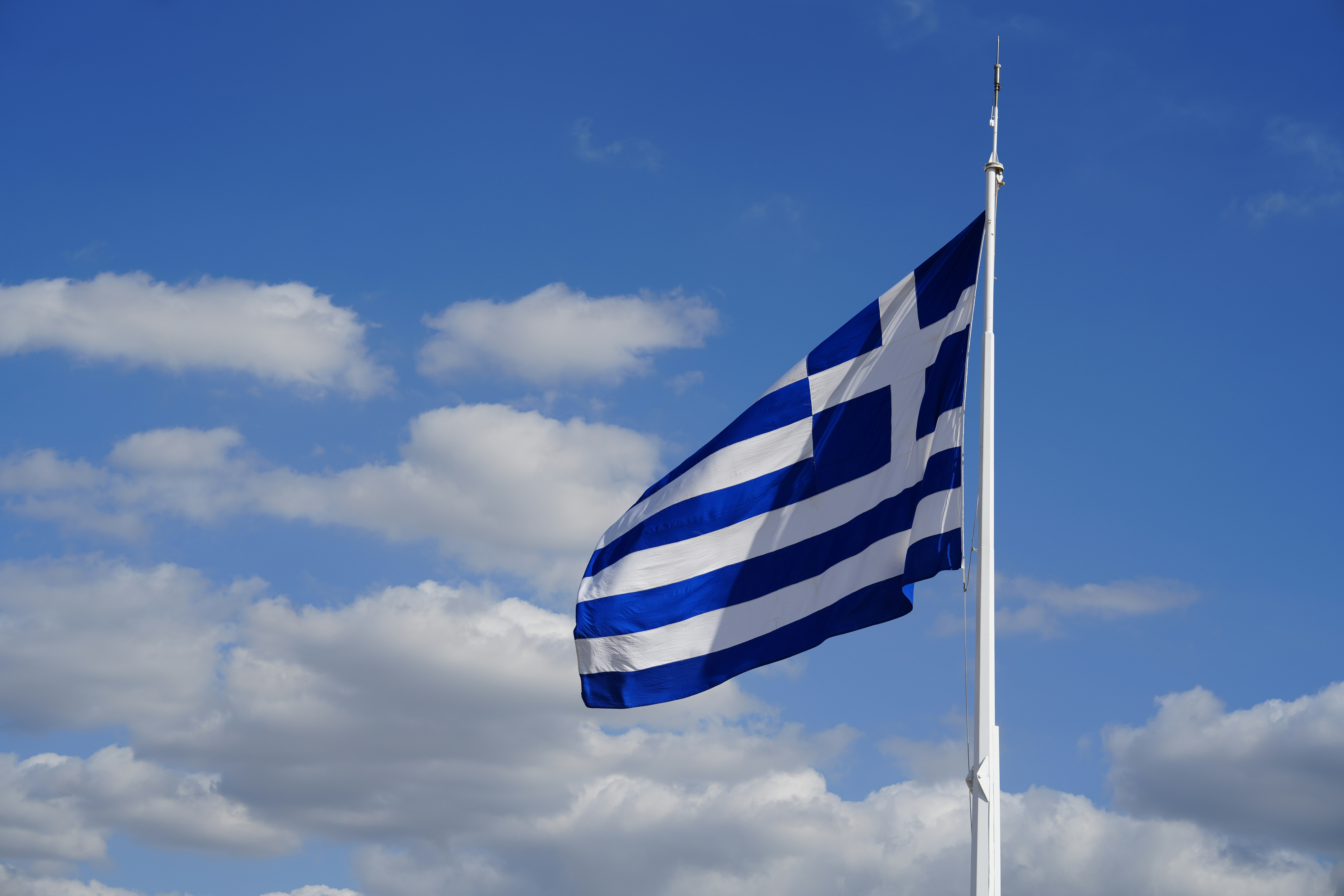 The greek flag waves against a blue sky.