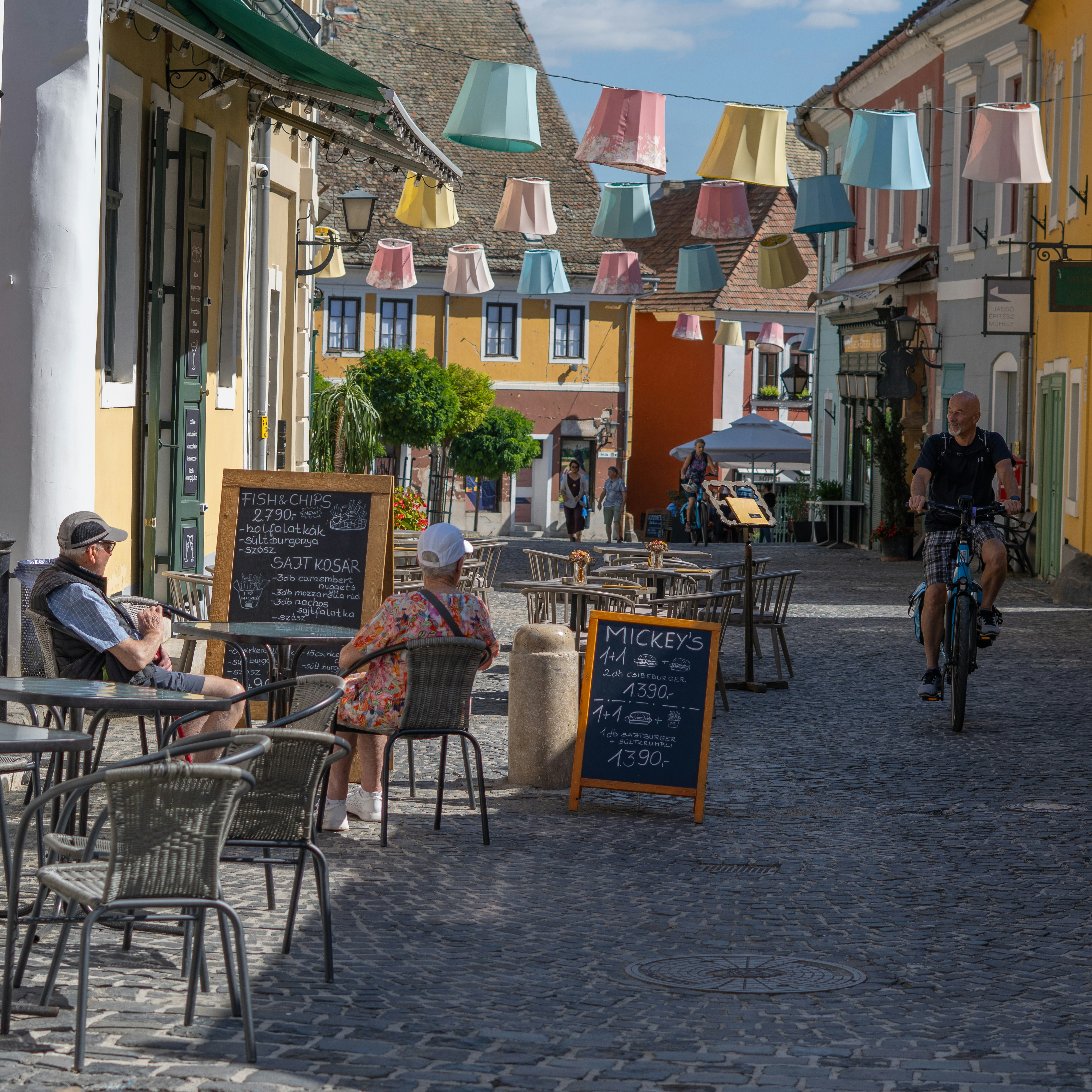 People sit at outdoor cafe tables on cobblestone street.