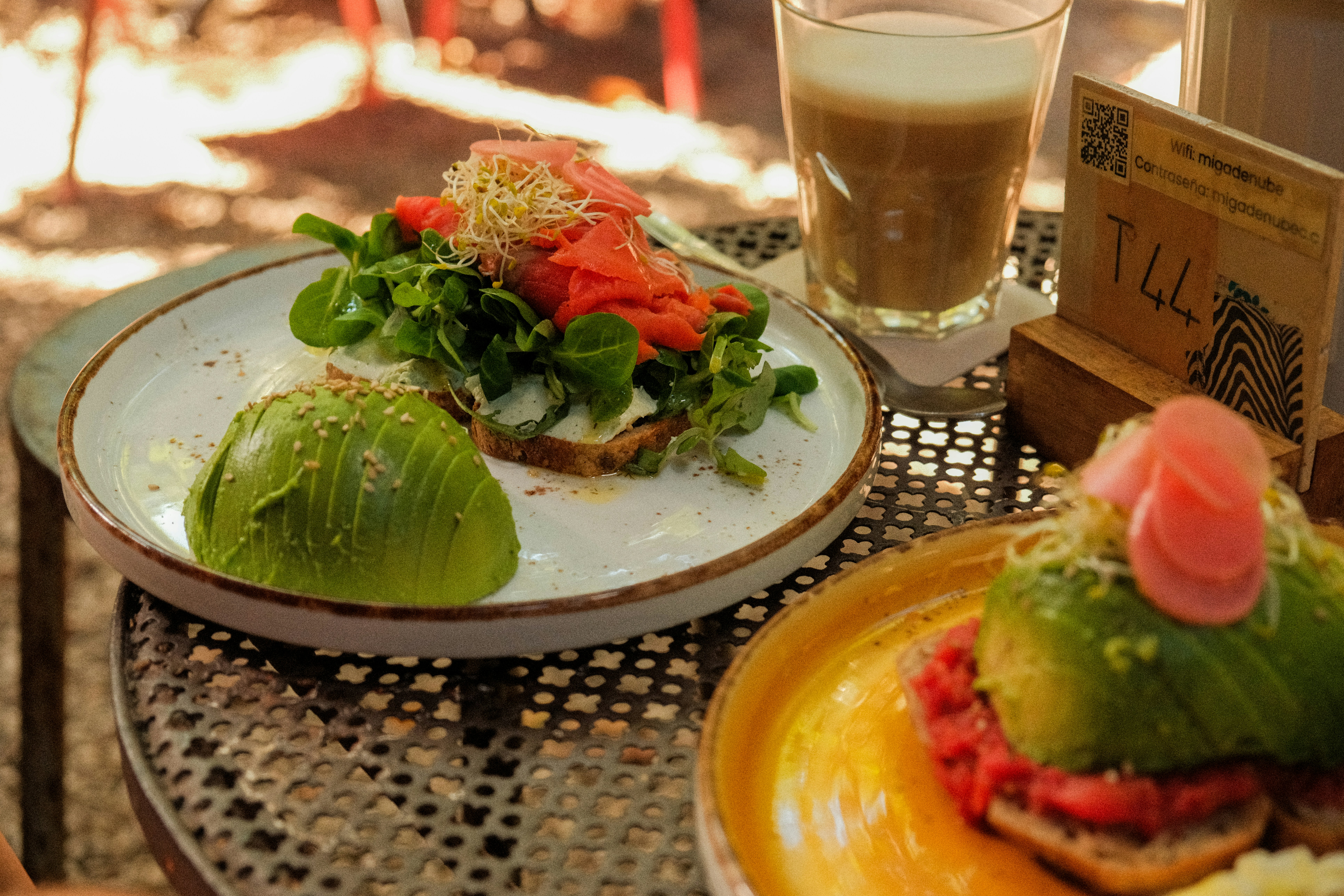 Pane tostato all'avocado con salmone e verdure, caffè latte vicino.