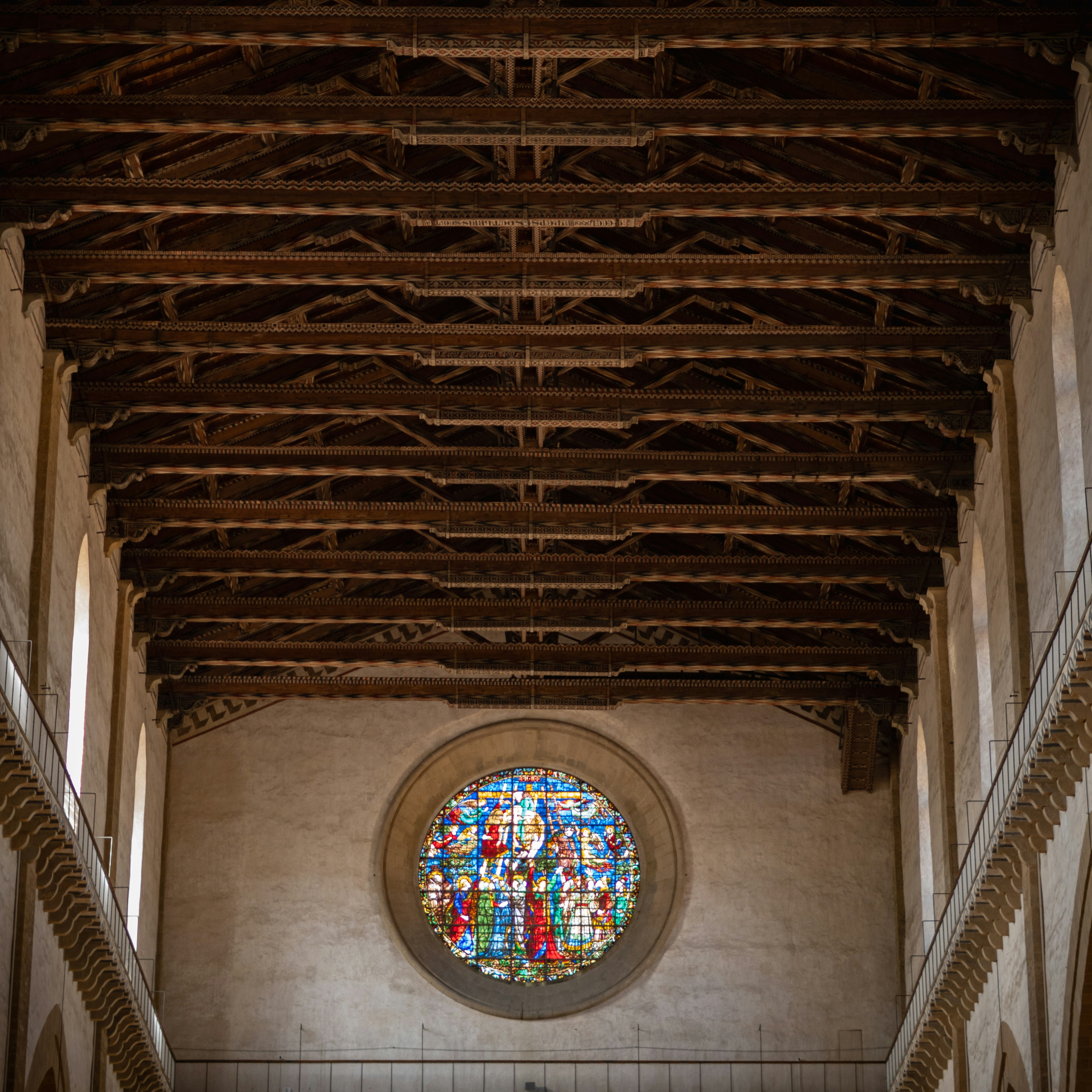 Wooden beamed ceiling above a circular stained glass window.