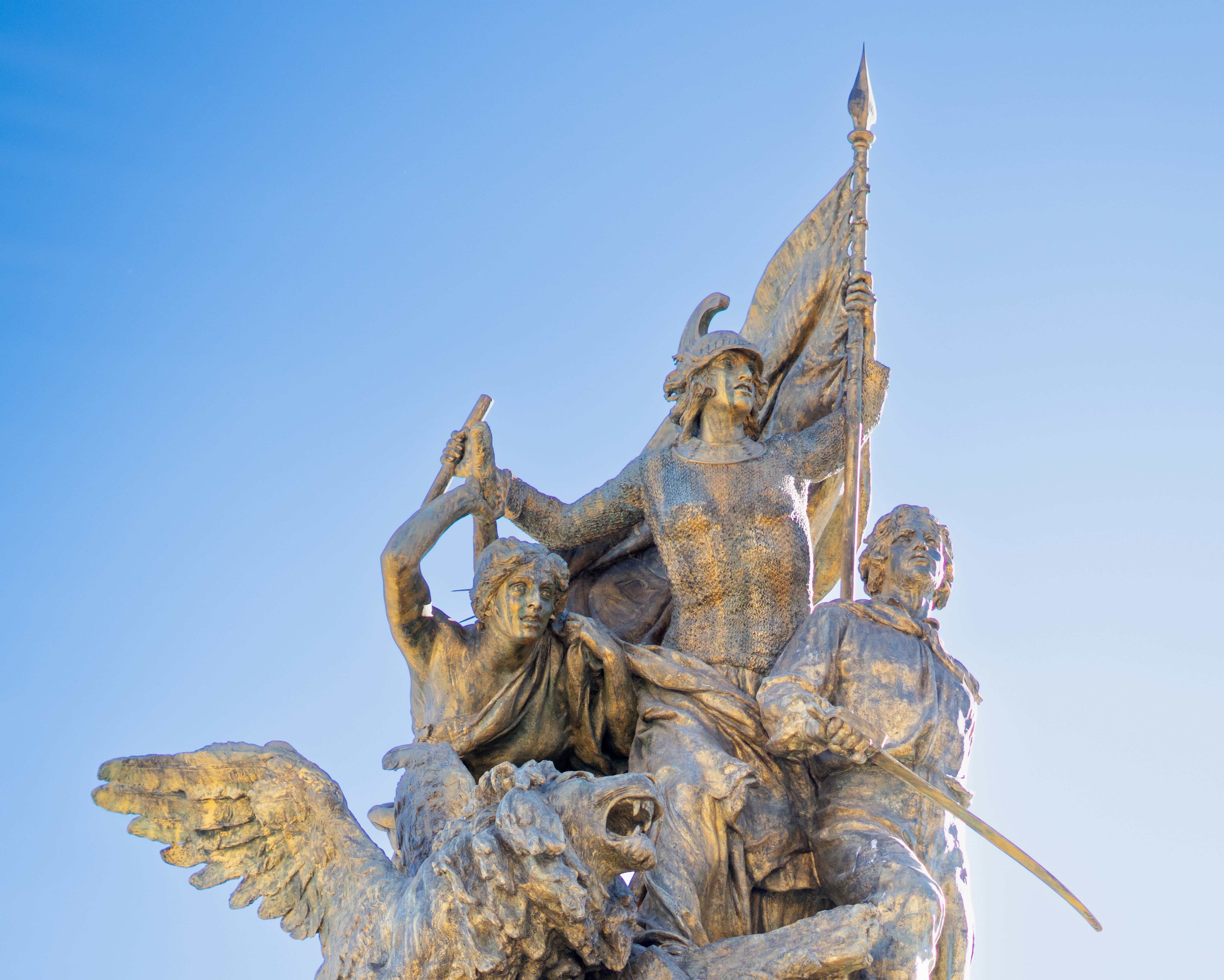 Bronze monument with figures and flag against sky