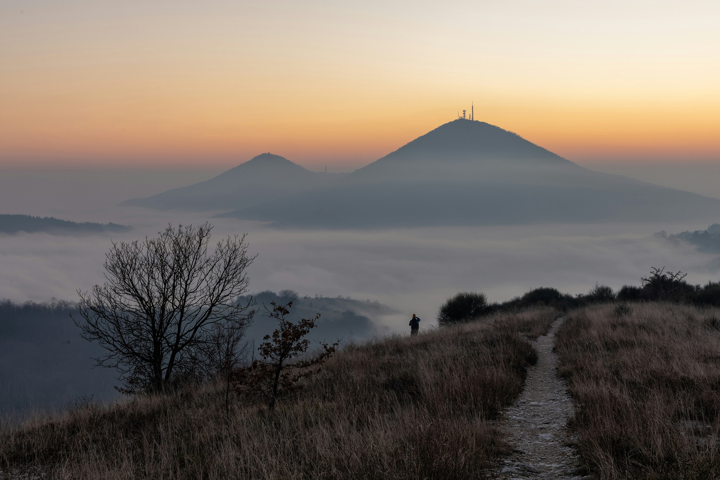 Neblige Berglandschaft bei Sonnenaufgang mit einem einsamen Wanderer.