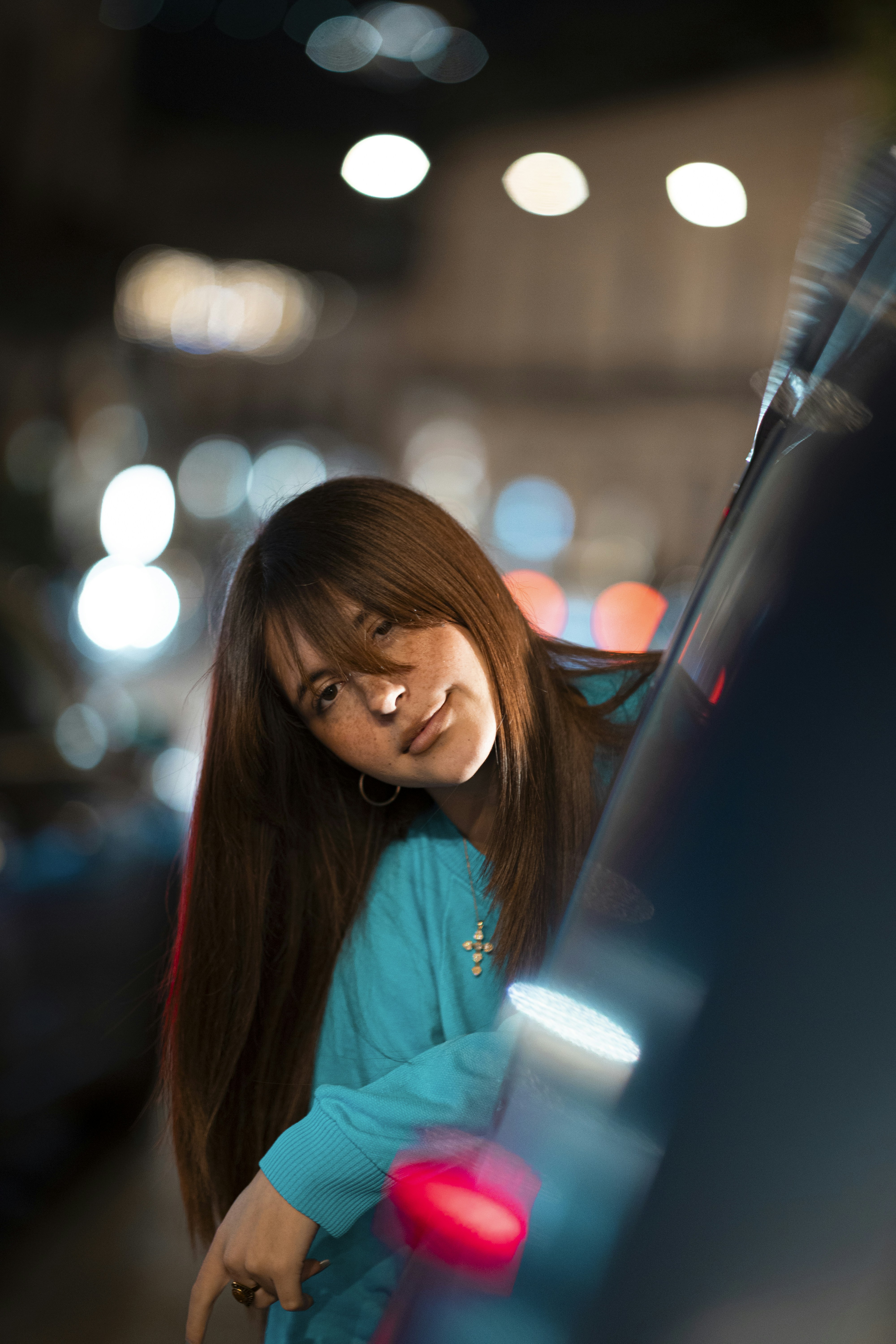 Woman with long brown hair leaning on car at night