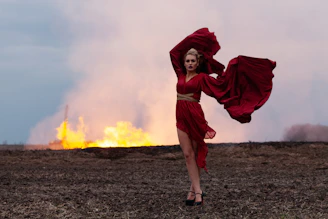 Woman in red dress stands in front of a fire
