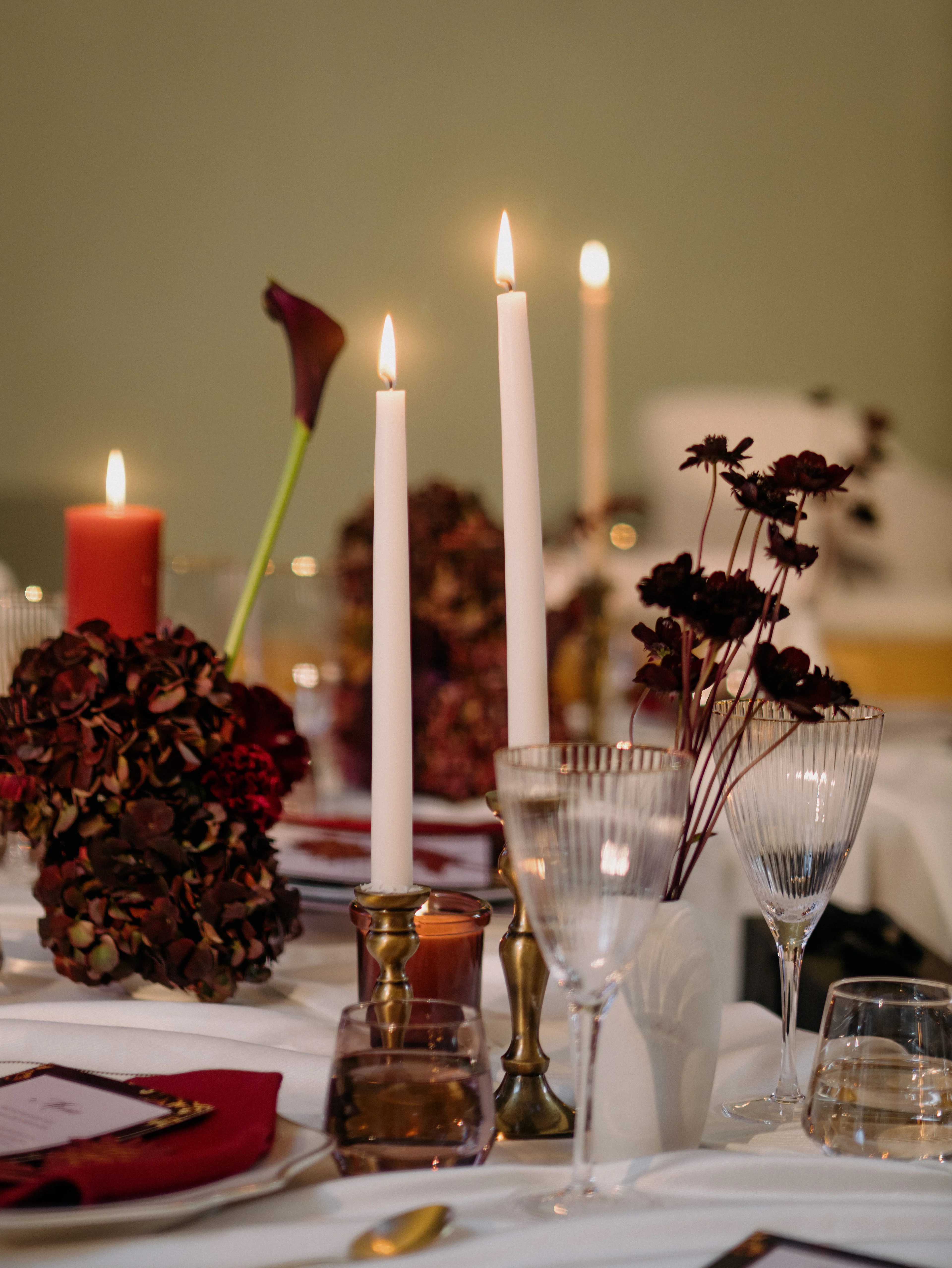 Tall white candles, red roses and dark florals on a dinner table